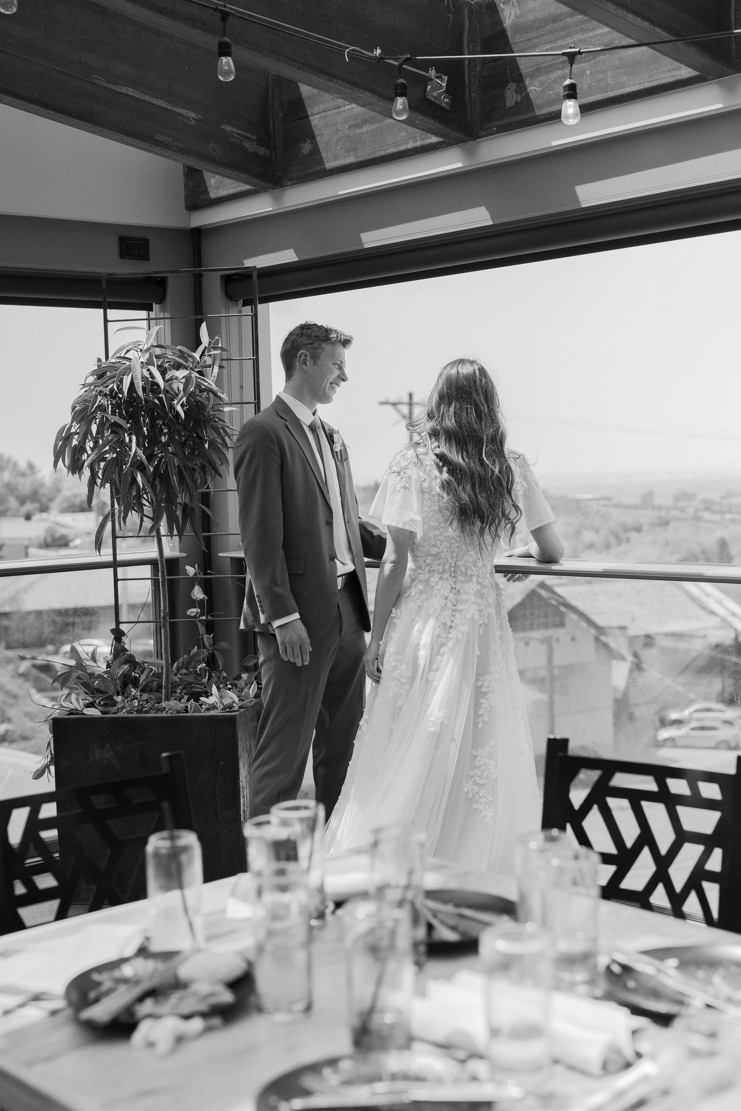 Black and white photo of bride and groom sharing a romantic moment on a decorated venue balcony with scenic views.