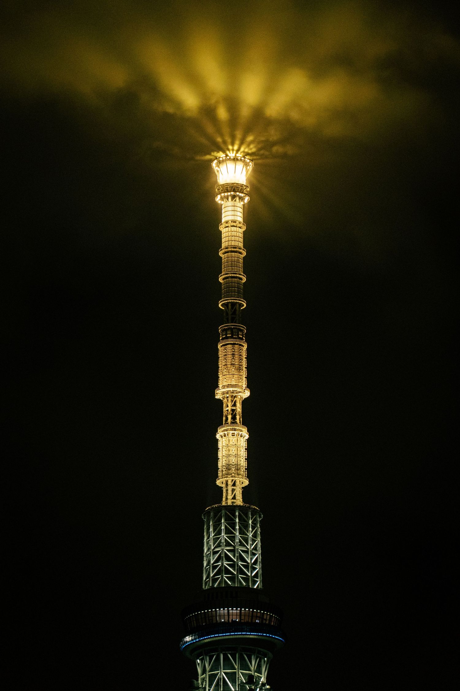 A tall, illuminated tower with a bright light shining from the top against a dark background.