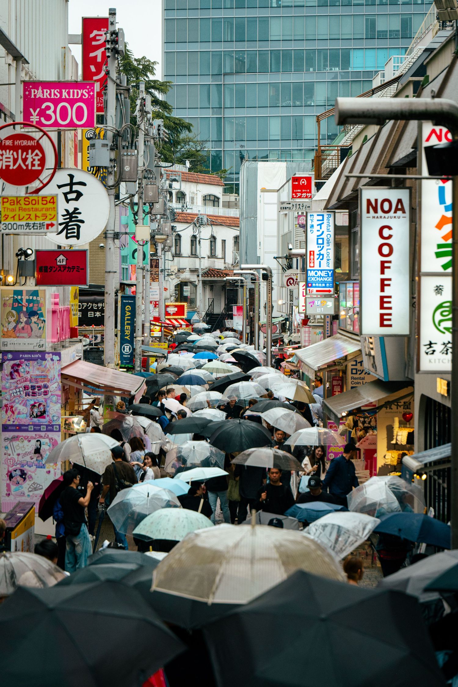 A crowded street in a bustling Japanese city, with umbrellas shielding pedestrians from the rain.