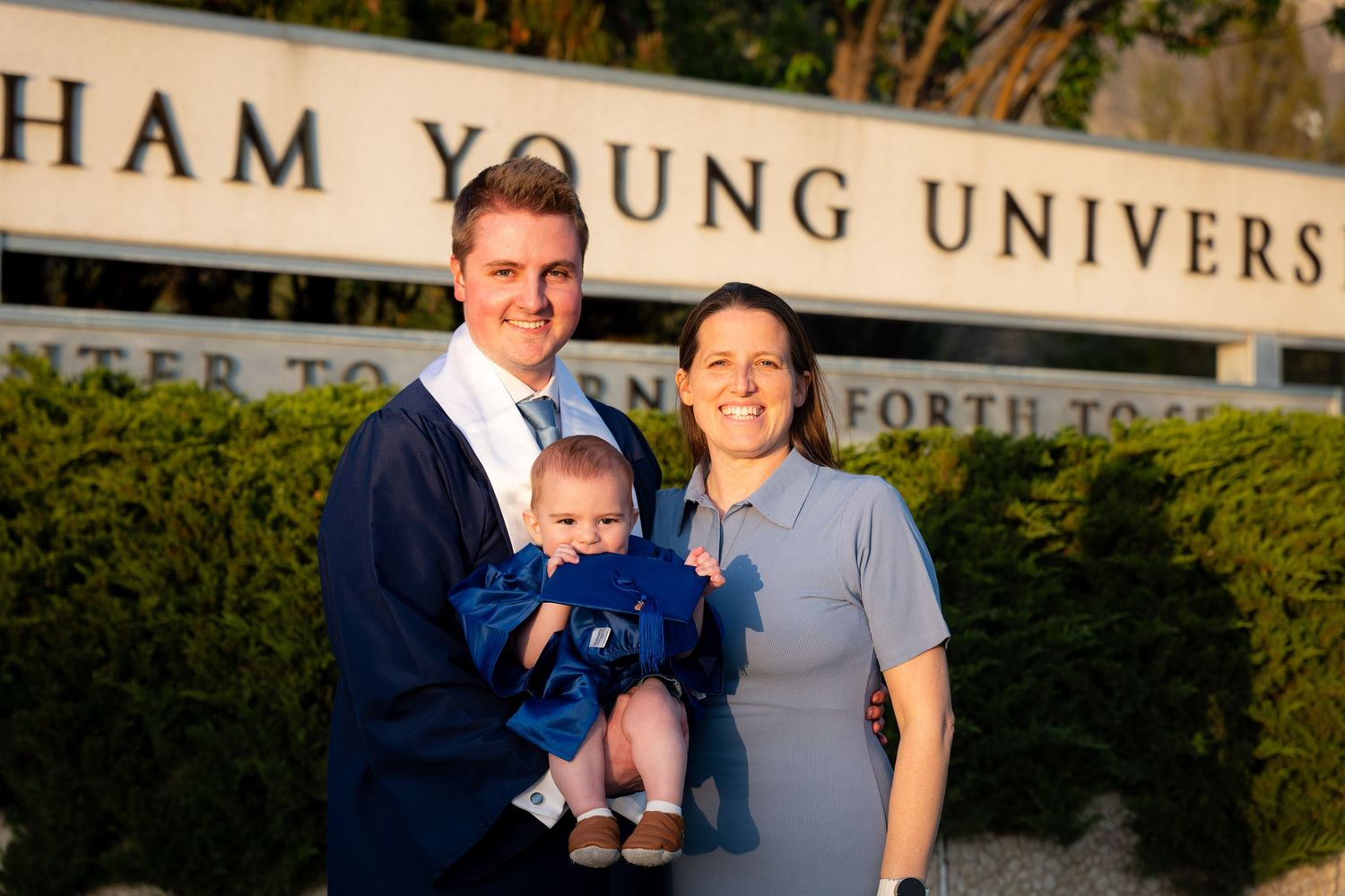 A family, including a man, woman, and baby, stand in front of a university building.