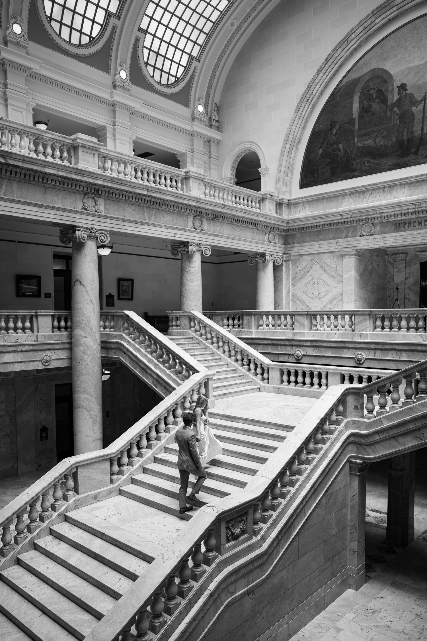 Black and white photo of a grand staircase in a neoclassical building with ornate columns and balustrades.