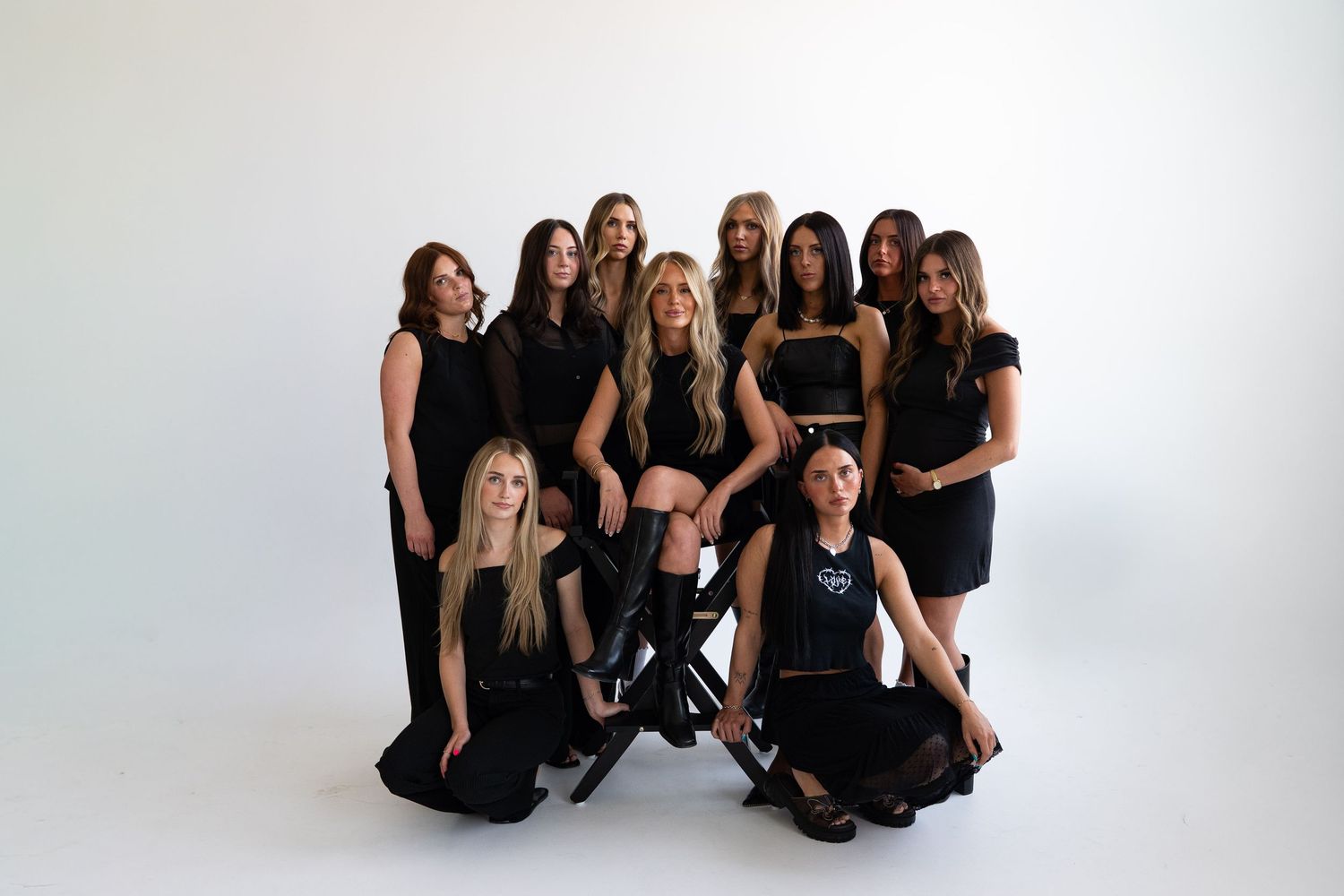Group of ten women posing together in matching black outfits against a white background in a professional photo shoot.