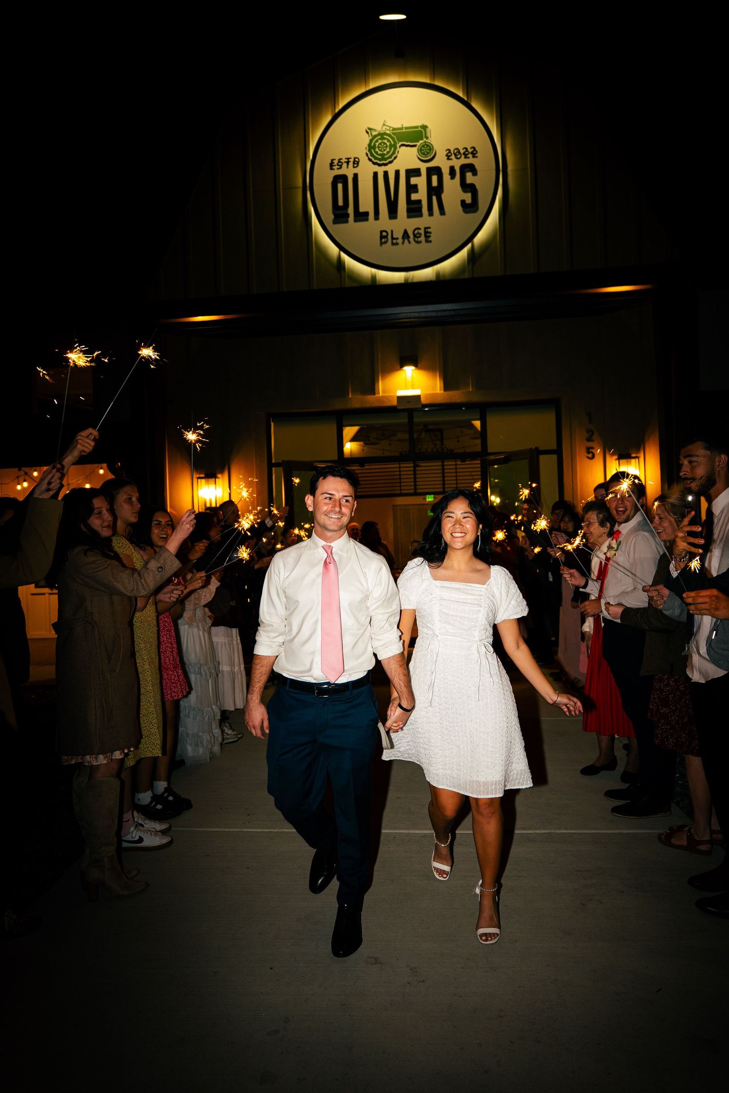 Newlyweds exit Oliver's Place venue through sparkler send-off at night wedding reception.