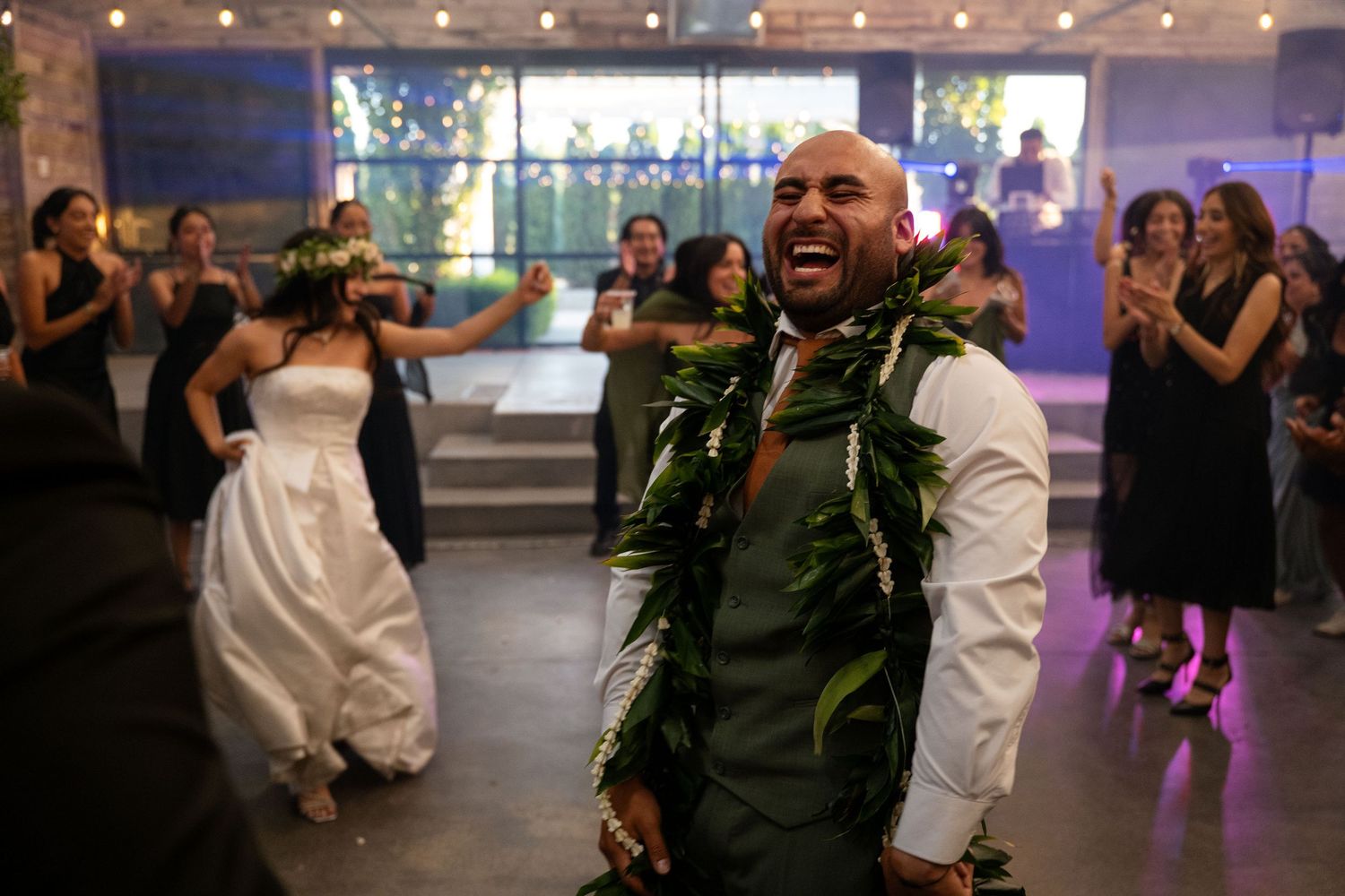 Joyful groom laughing during wedding reception dance floor celebration with bride and guests in elegant venue.