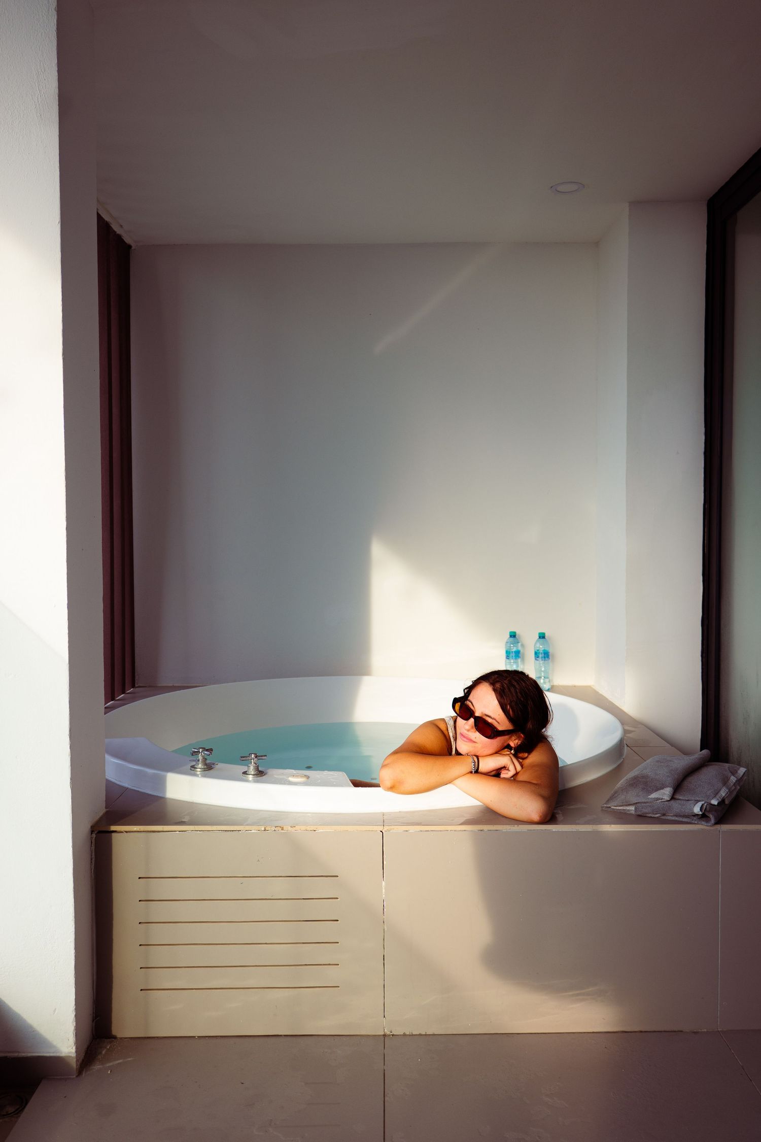 A woman relaxes in a bathtub, surrounded by candles and greenery.