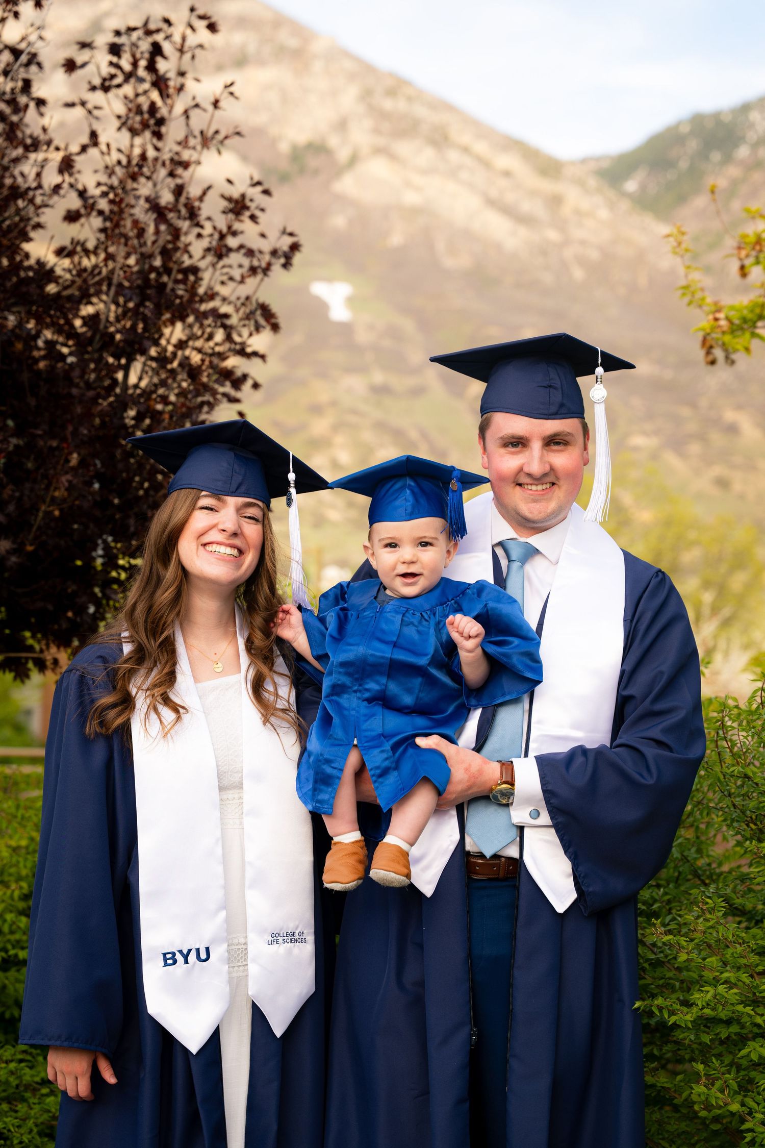 A family, including a woman, man, and baby, stand together in front of a university building.