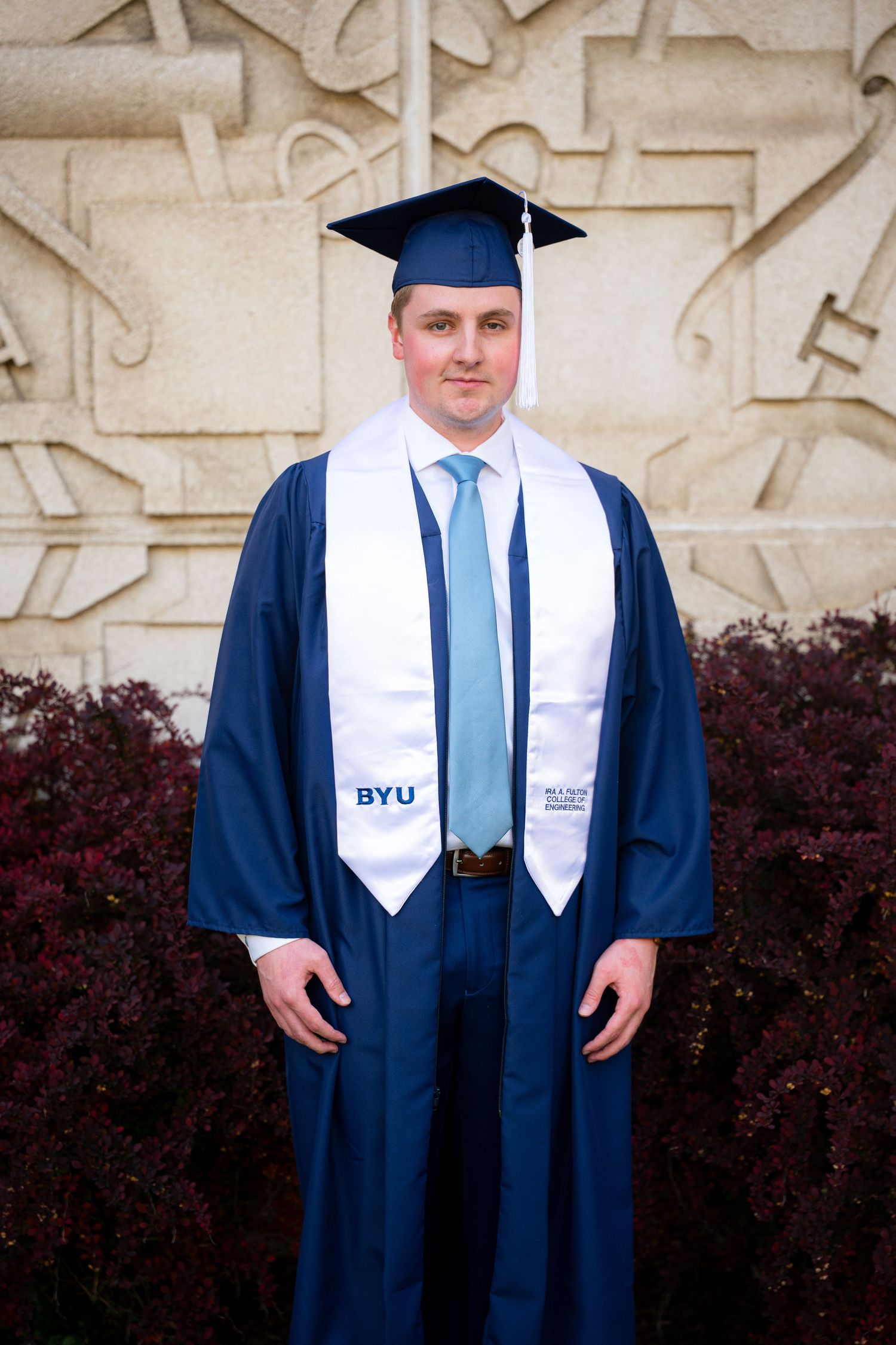 A woman in a graduation gown and cap stands in front of a university building.