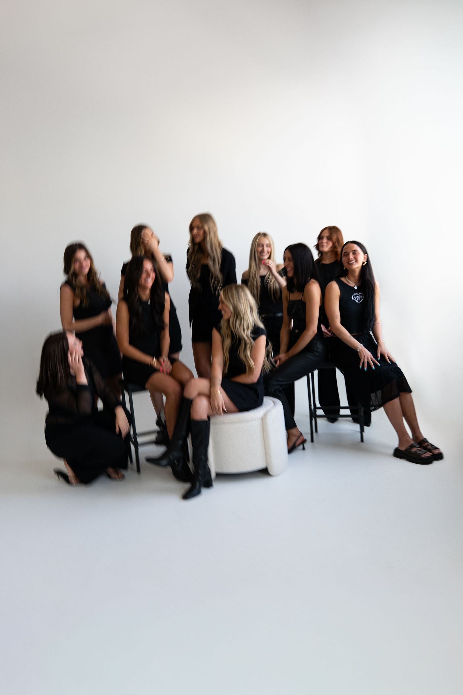 Group of women in matching black outfits posing together on chairs in a bright white studio setting.