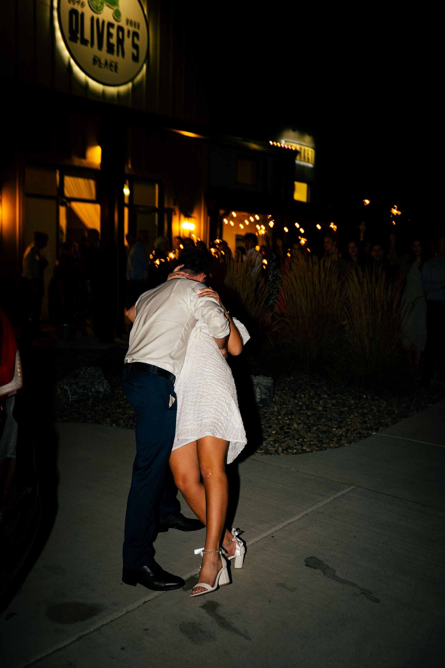 Bride and groom embracing passionately outside Oliver's Place venue during nighttime wedding reception.