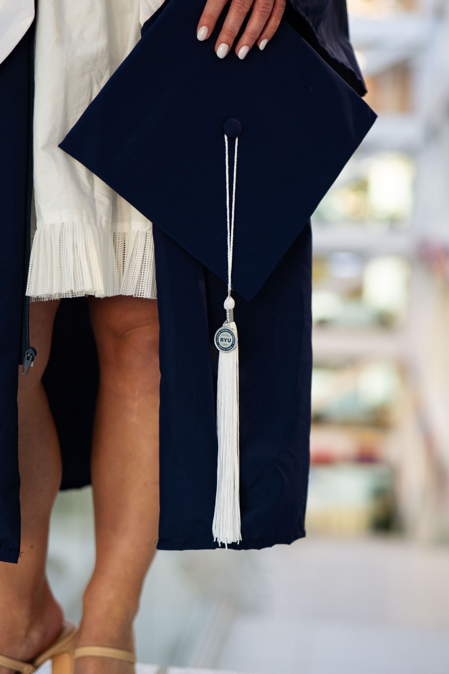 Graduate holding navy blue mortarboard cap with white tassel and silver charm at commencement ceremony.