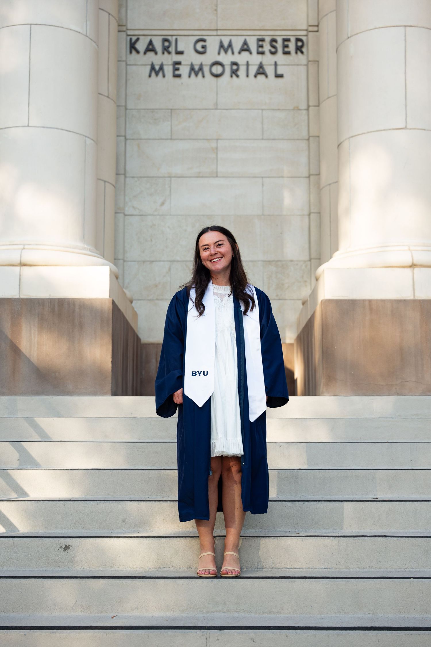 BYU graduate posing on steps of Karl G Maeser Memorial building in navy graduation gown.