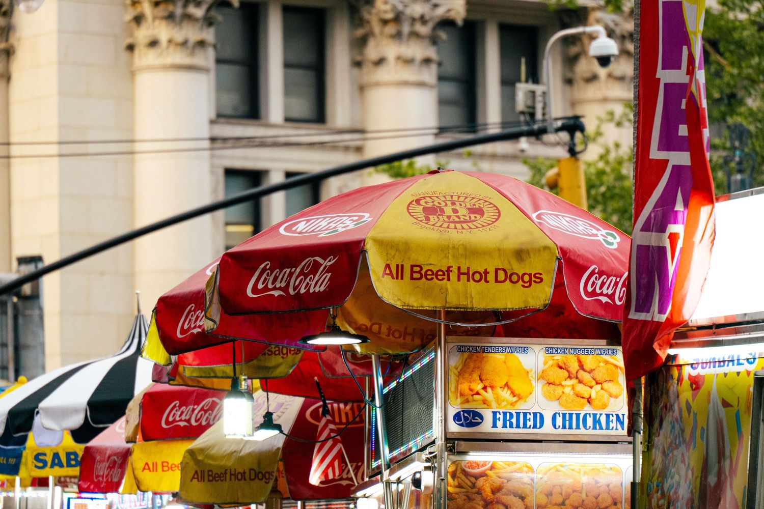 The image depicts a bustling street scene in New York City, with various food and merchandise vendors set up along the sidewalk.