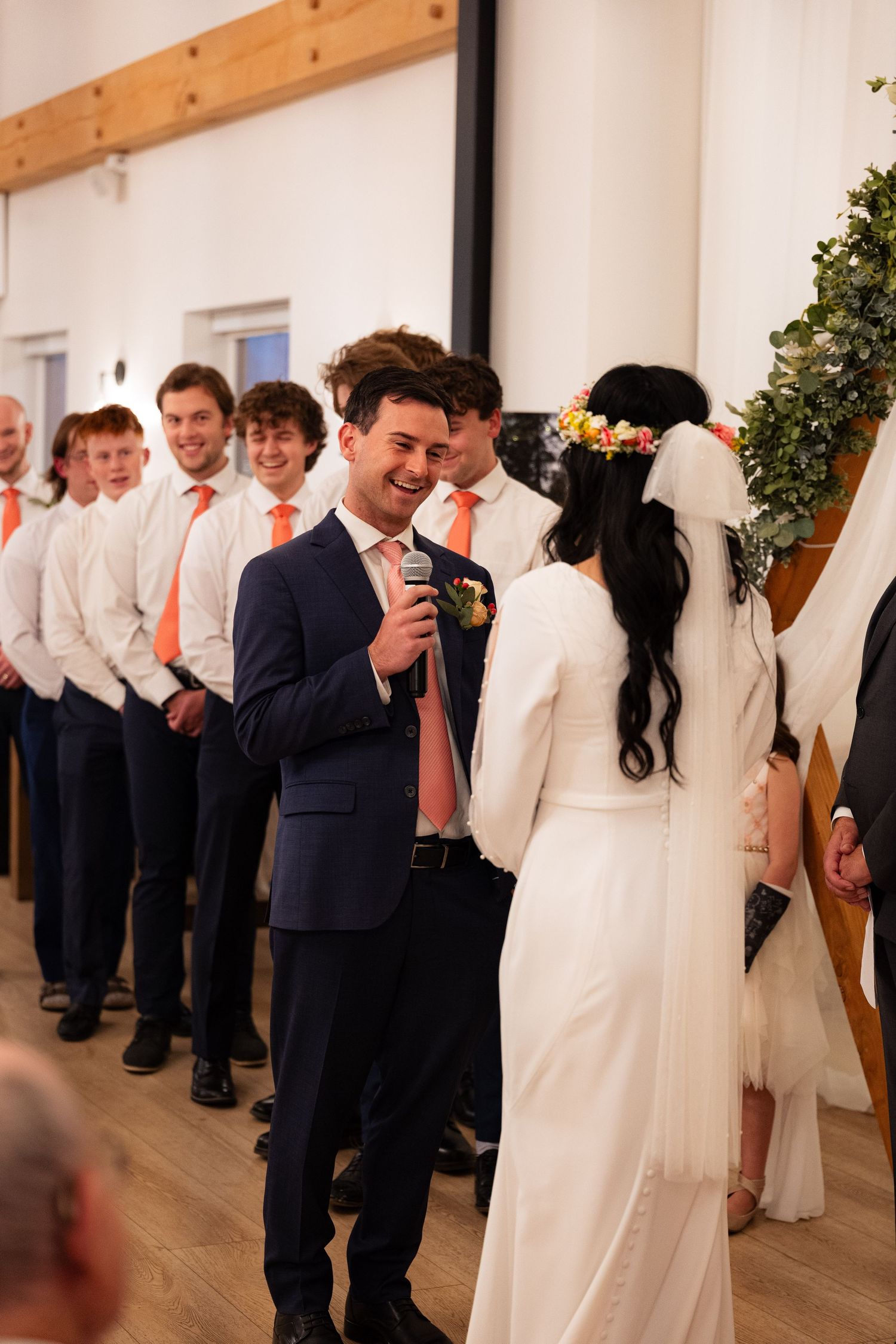 Groom laughing with bride at altar surrounded by groomsmen in orange ties.
