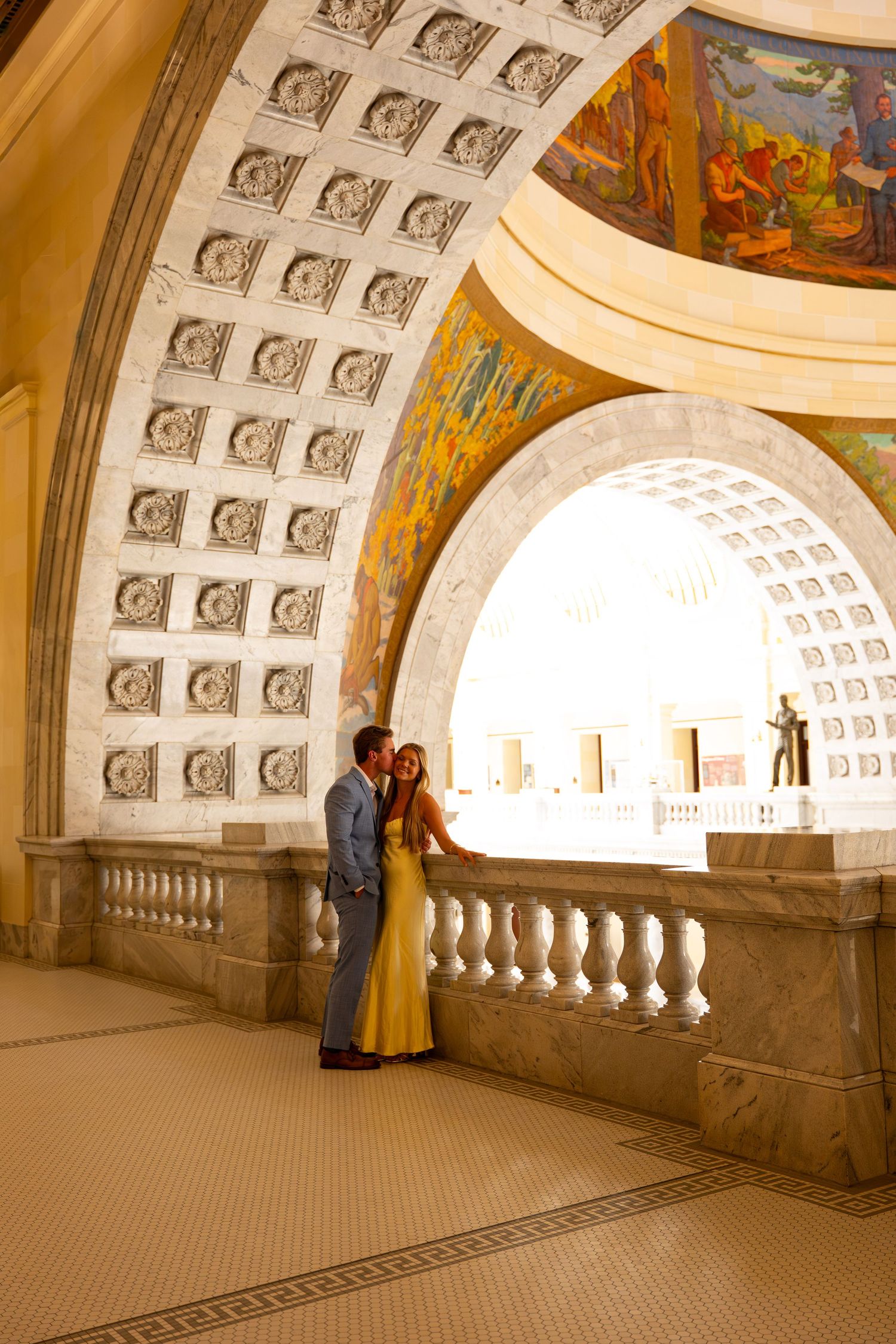 Couple sharing a romantic moment in an elegant domed building with ornate arches and colorful murals.