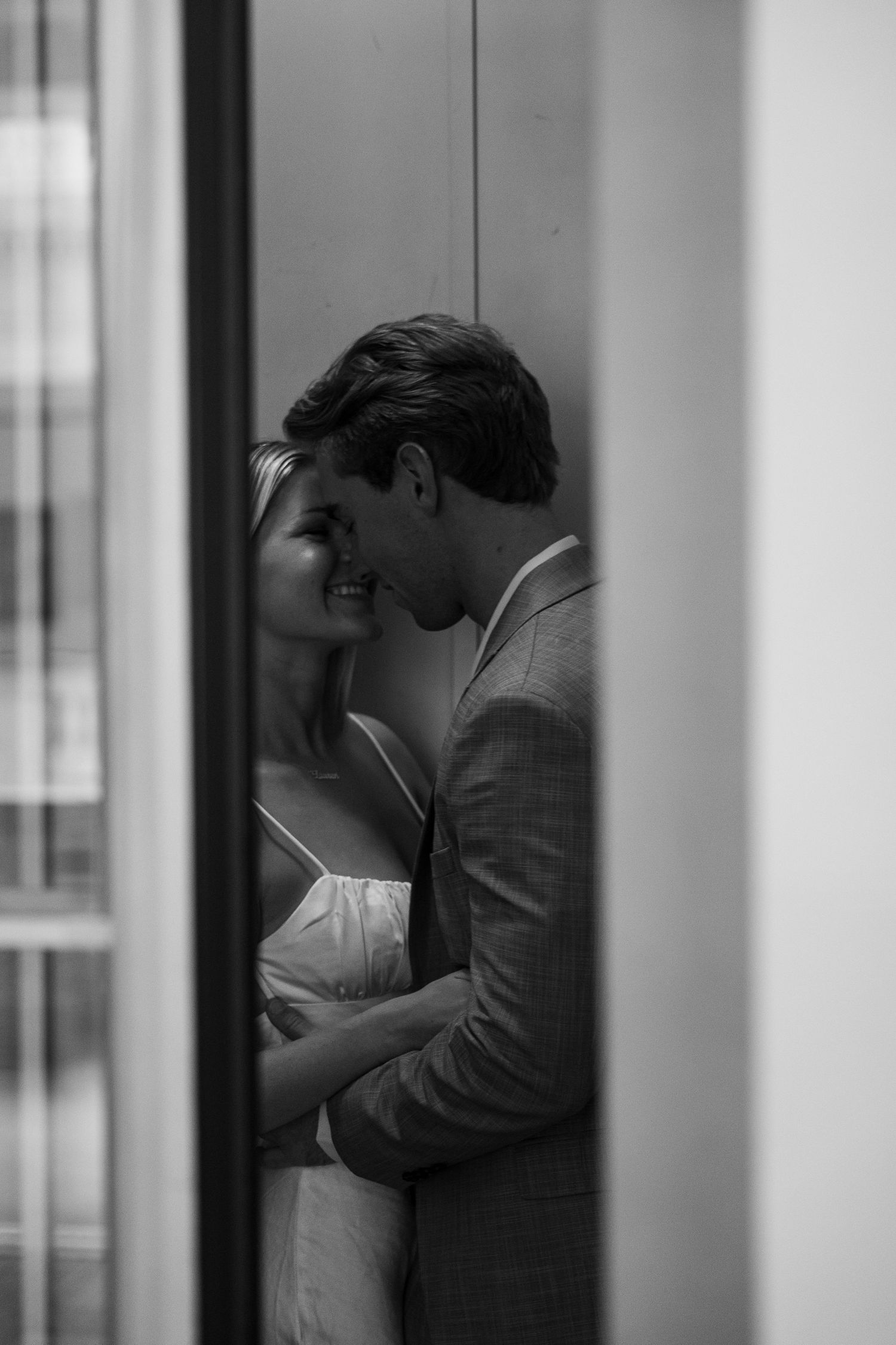 Black and white photo of a romantic couple embracing and smiling at each other in a doorway.