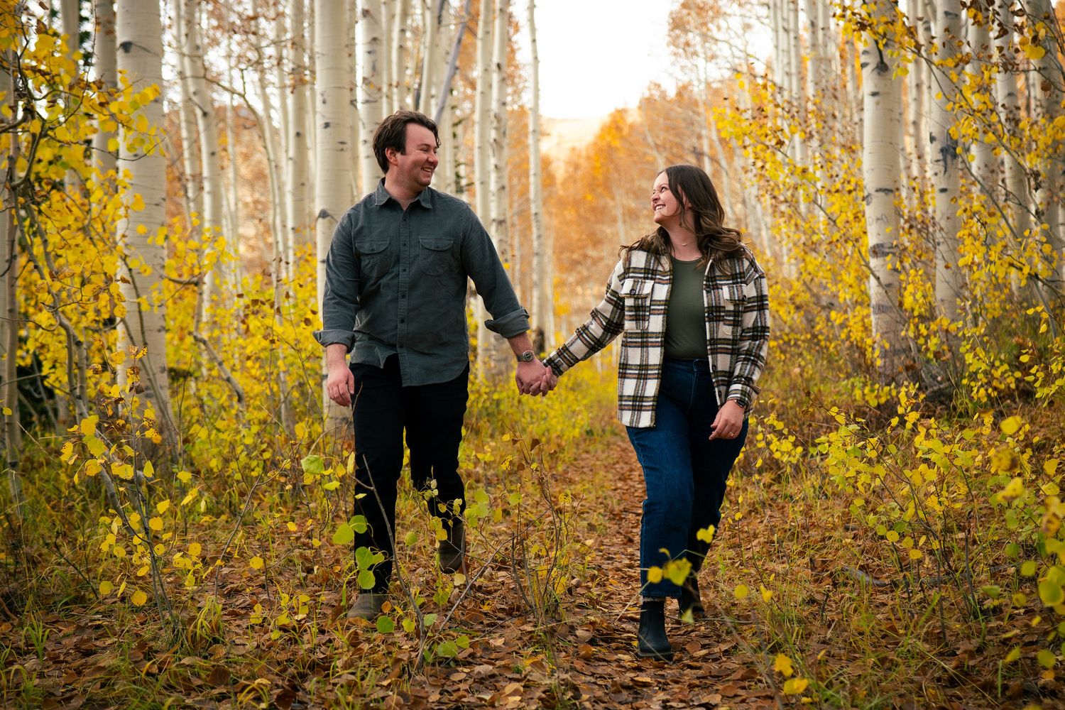 The image shows a couple walking together in a forest with fall foliage.