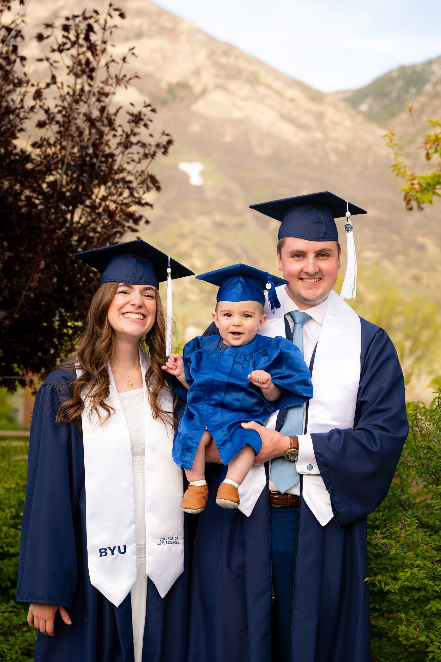 A family, including a couple and a young child, stand together in a grassy outdoor setting.