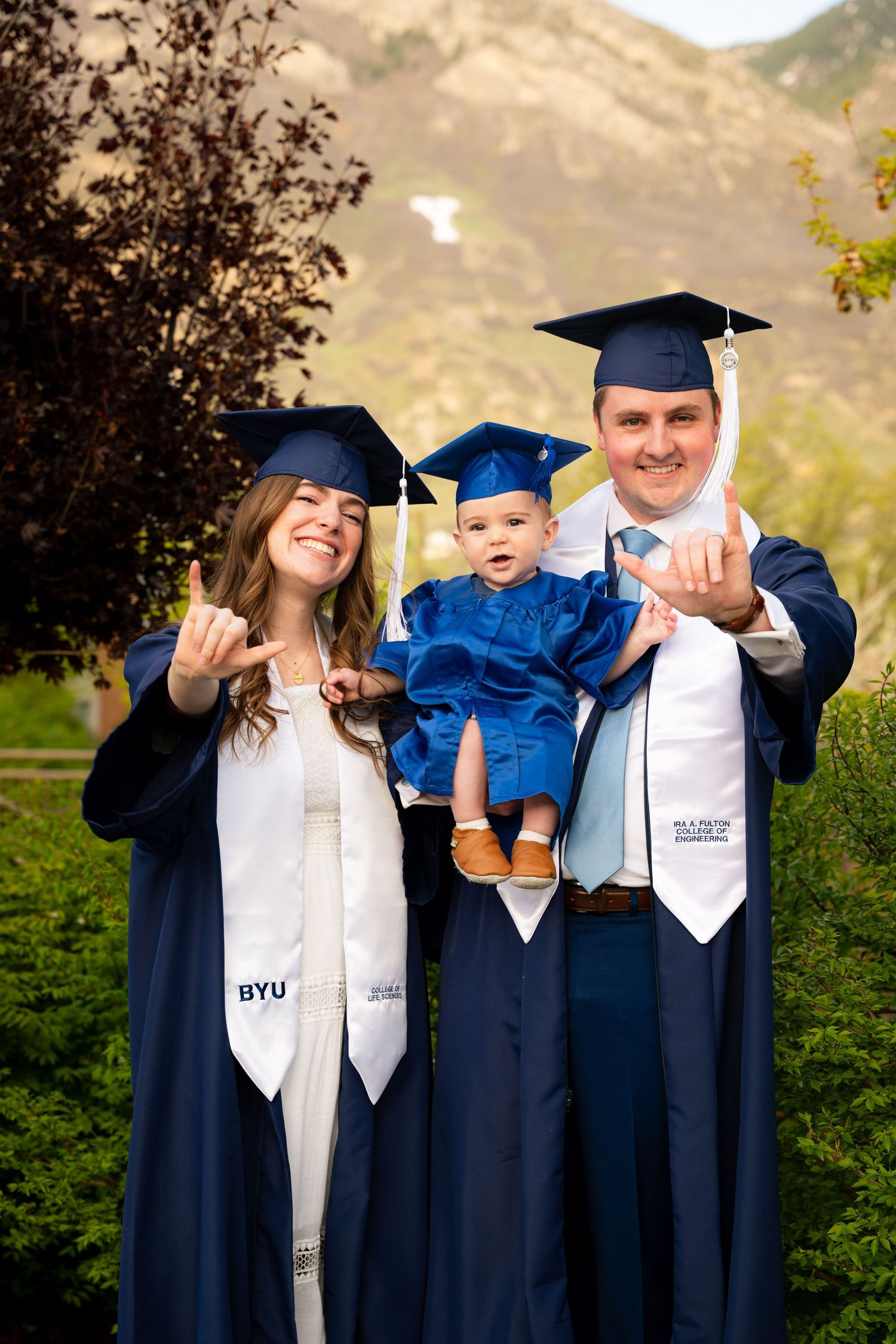 A family, including a woman, man, and baby, stand together in front of a university building.