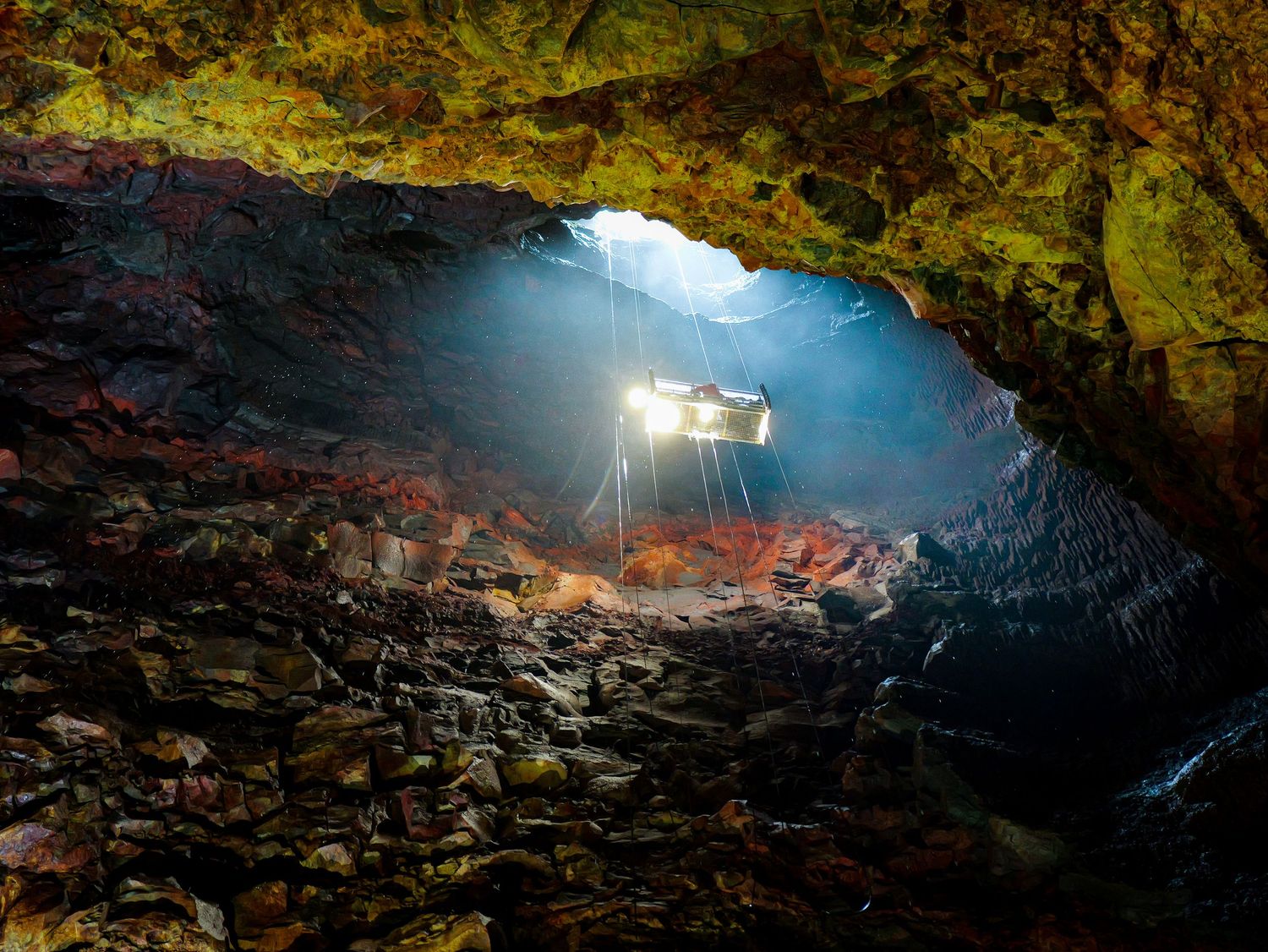 A person explores a dimly lit cave with a flashlight, revealing the natural rock formations and water inside.