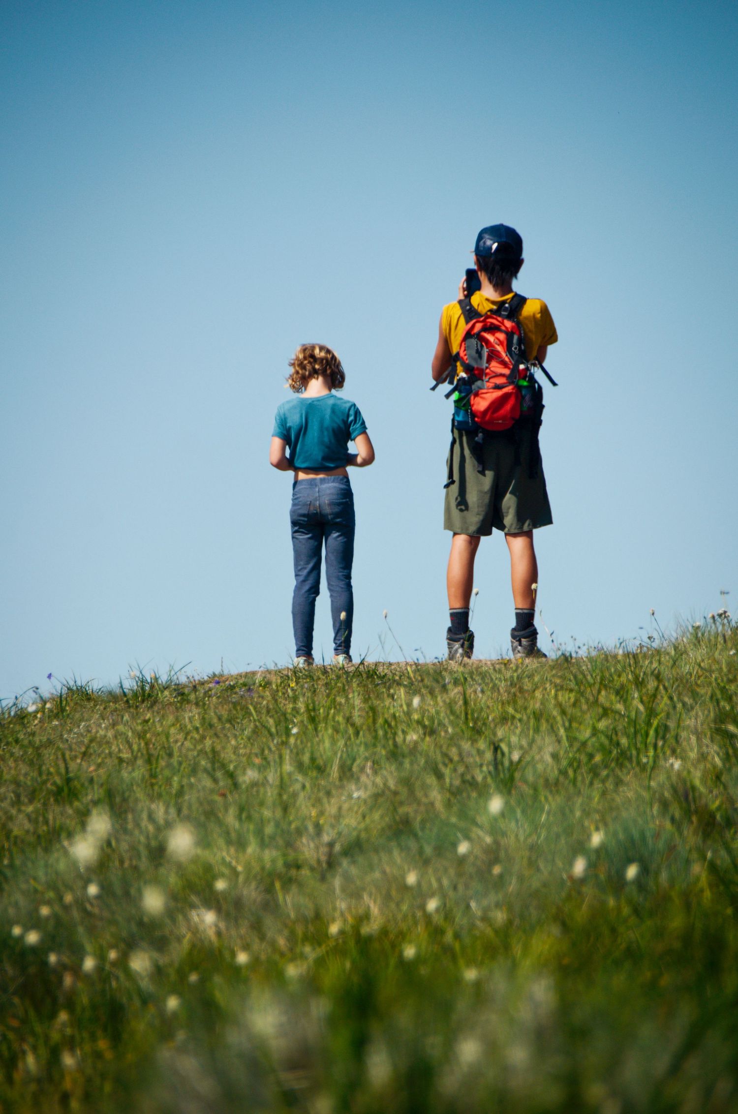 Two people, a man and a woman, standing on a grassy hill overlooking a scenic landscape.