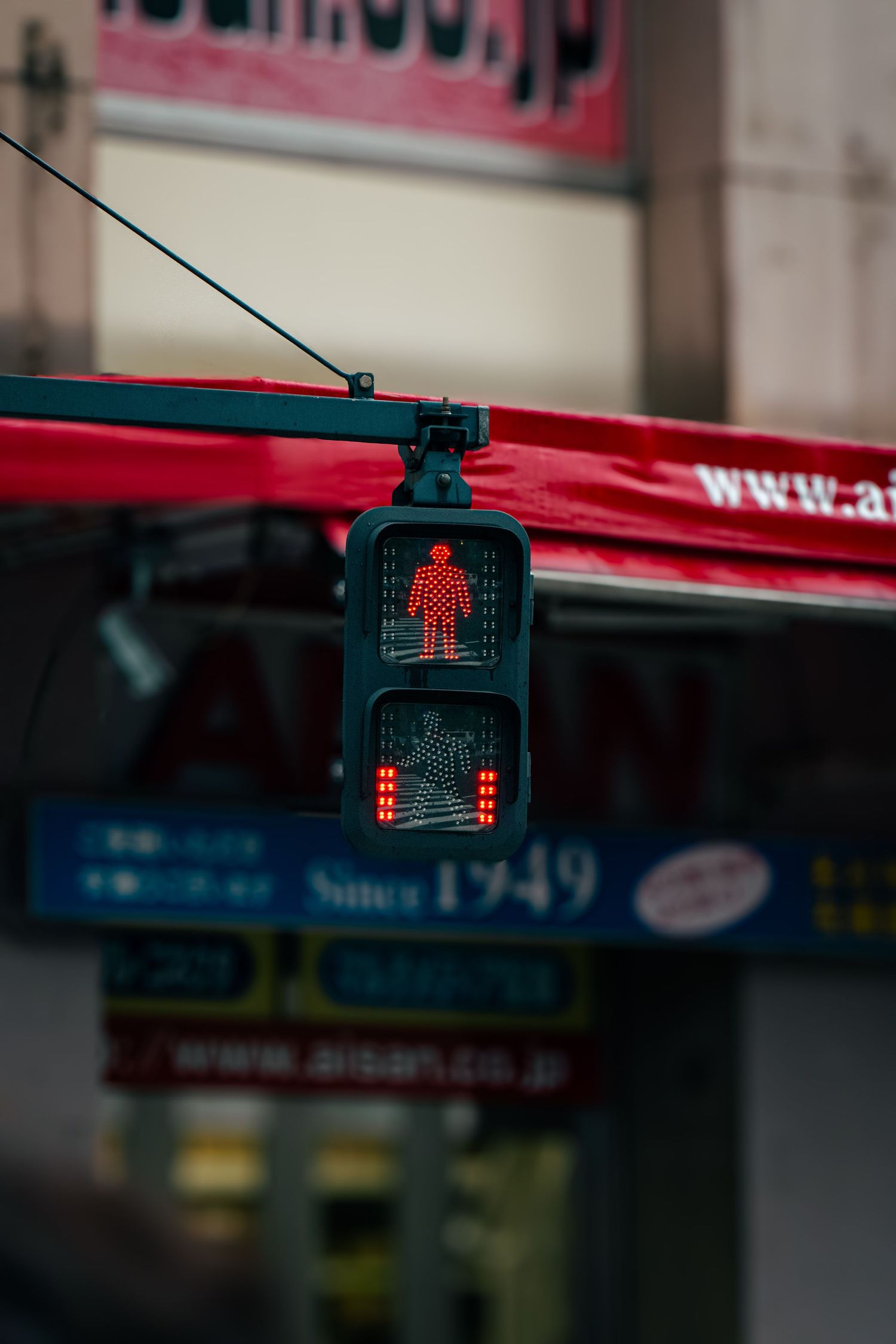A traffic light with a pedestrian crossing signal in a crowded city street in Japan.