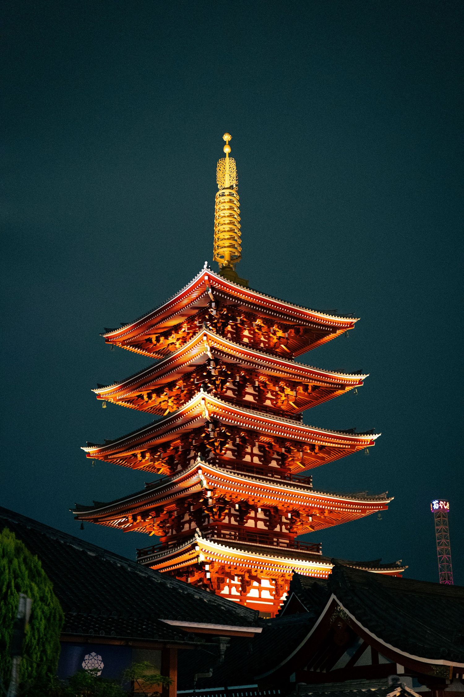 A tall, ornate Japanese pagoda tower illuminated at night against a dark background.