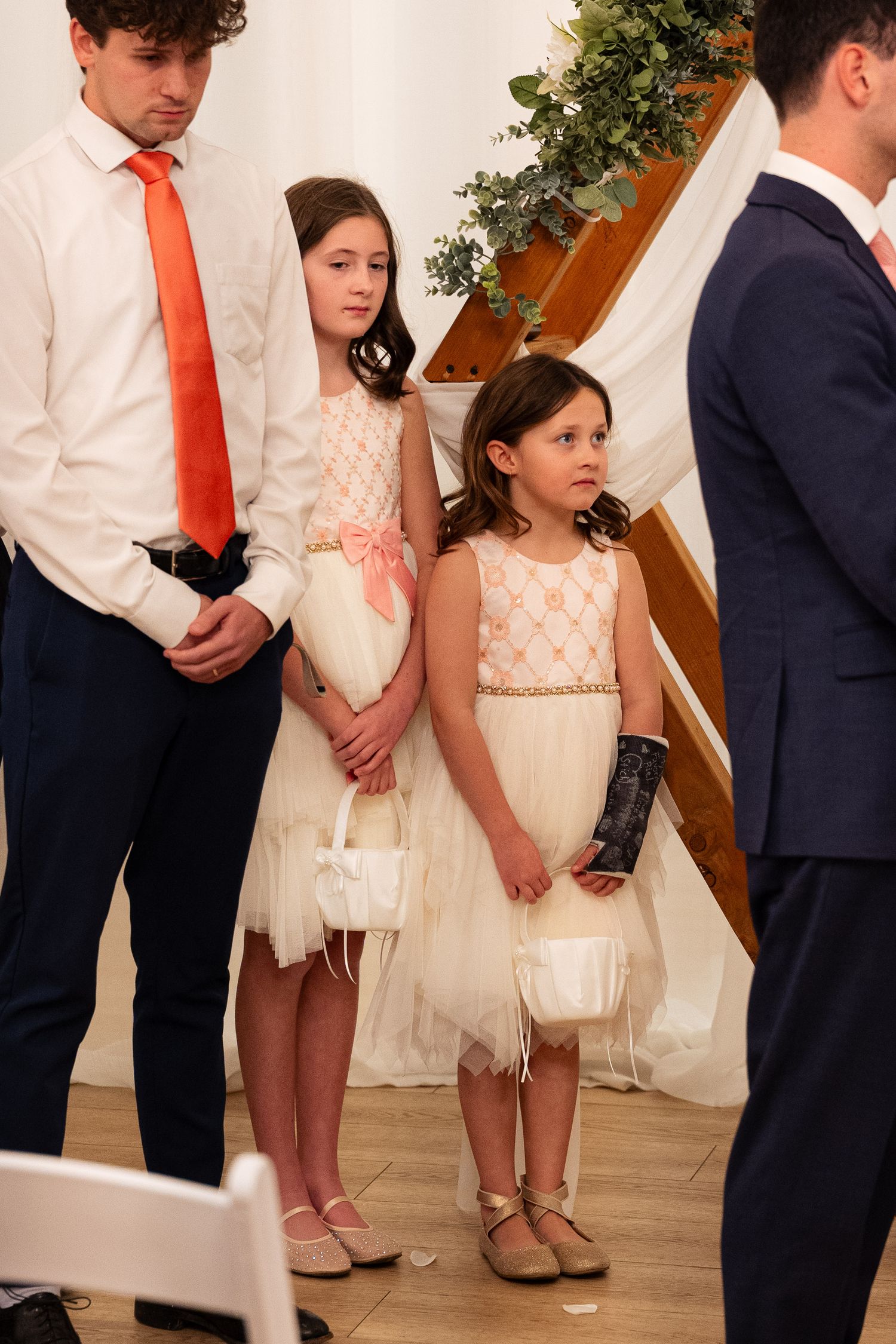 Two young flower girls in white dresses holding baskets at a wedding ceremony.