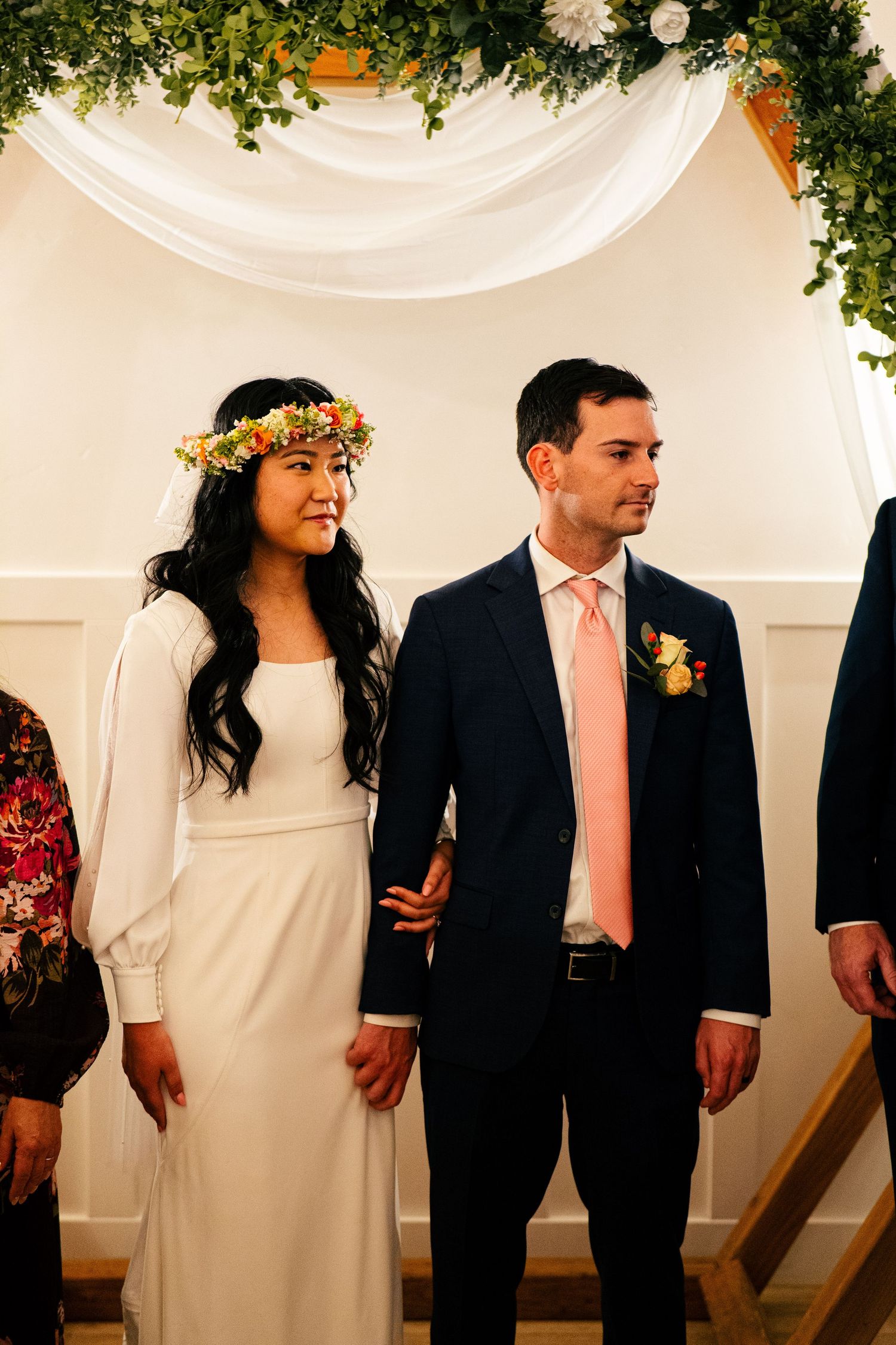 Bride wearing flower crown and groom in navy suit with peach tie at wedding altar.