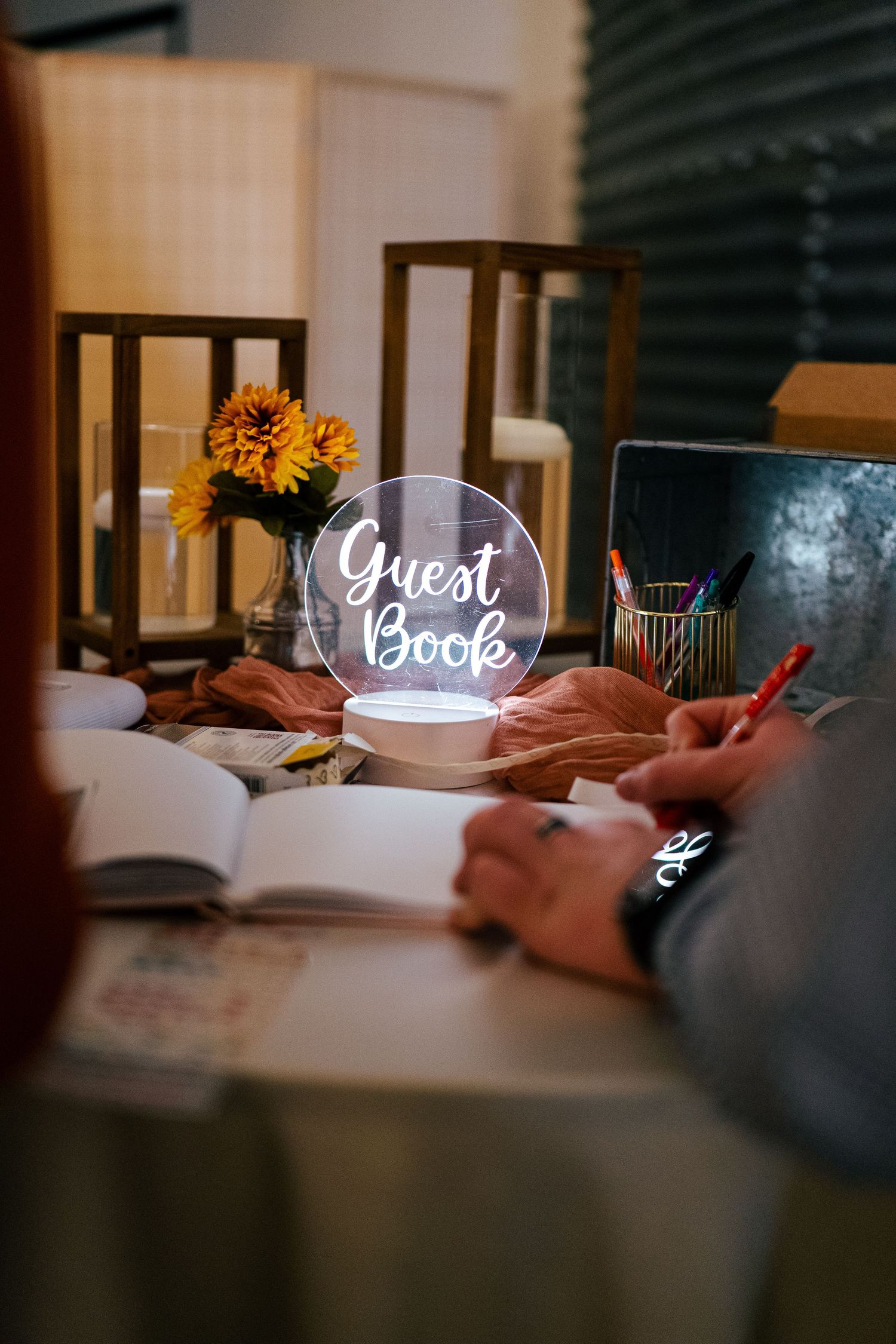 Illuminated Guest Book sign on table with sunflowers and open book at wedding reception.