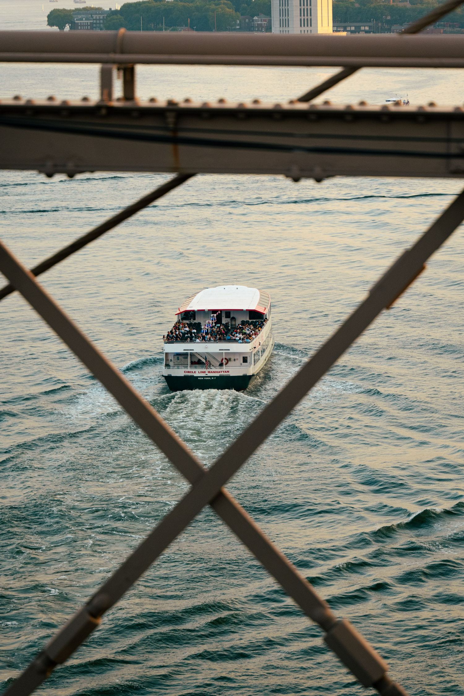 A small boat sailing on the waters of the harbor, seen through the metal frame of a bridge or structure.
