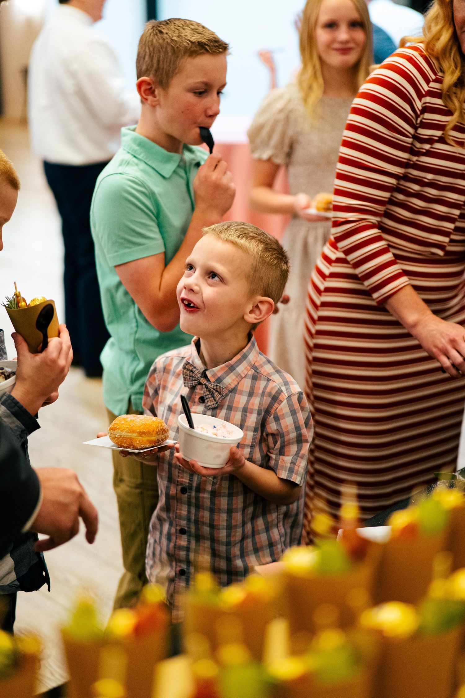 Young boy smiles while holding food at a casual wedding reception buffet table.
