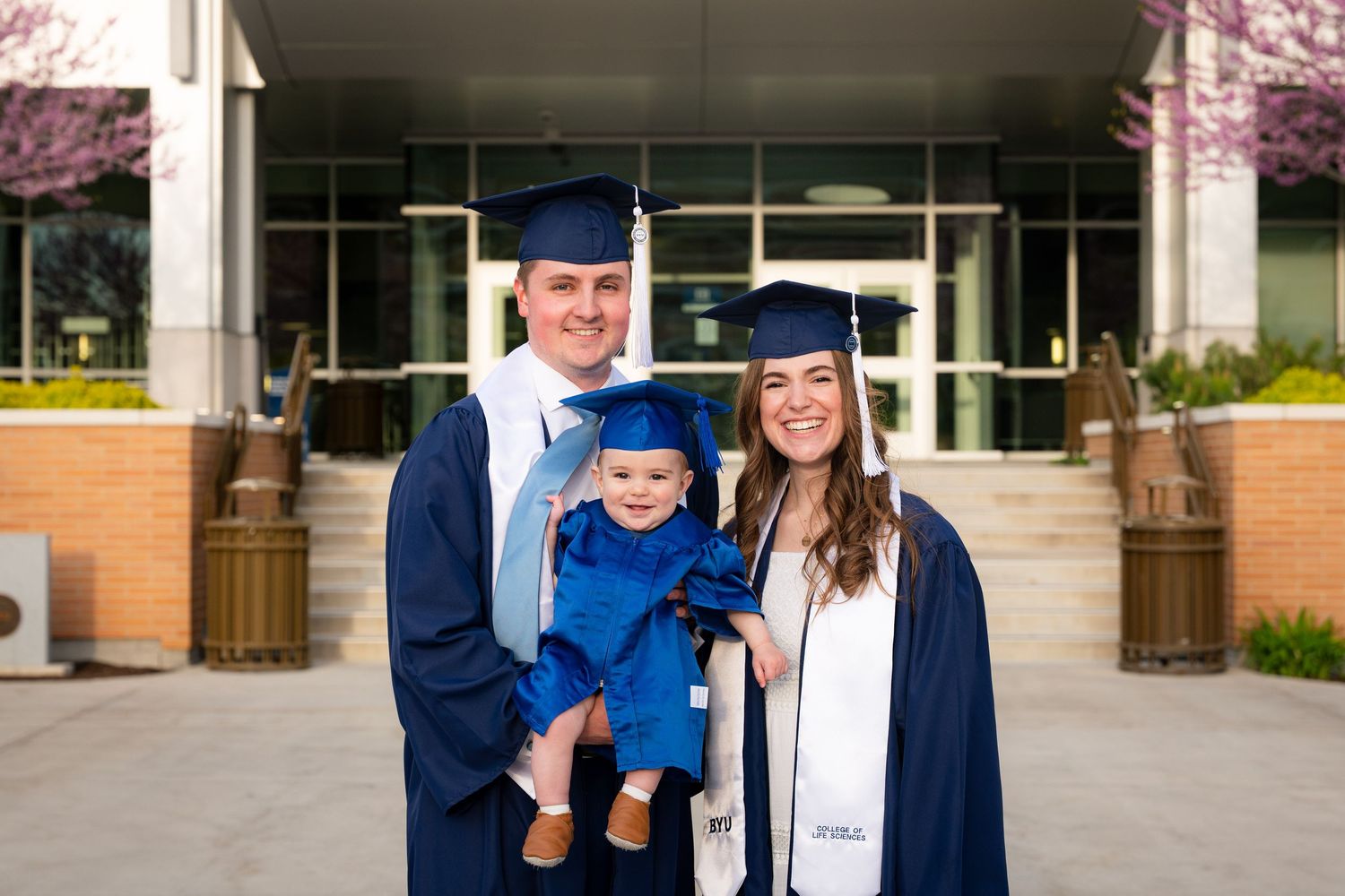 A family of three, a man, woman, and young child, stand in front of a university building.