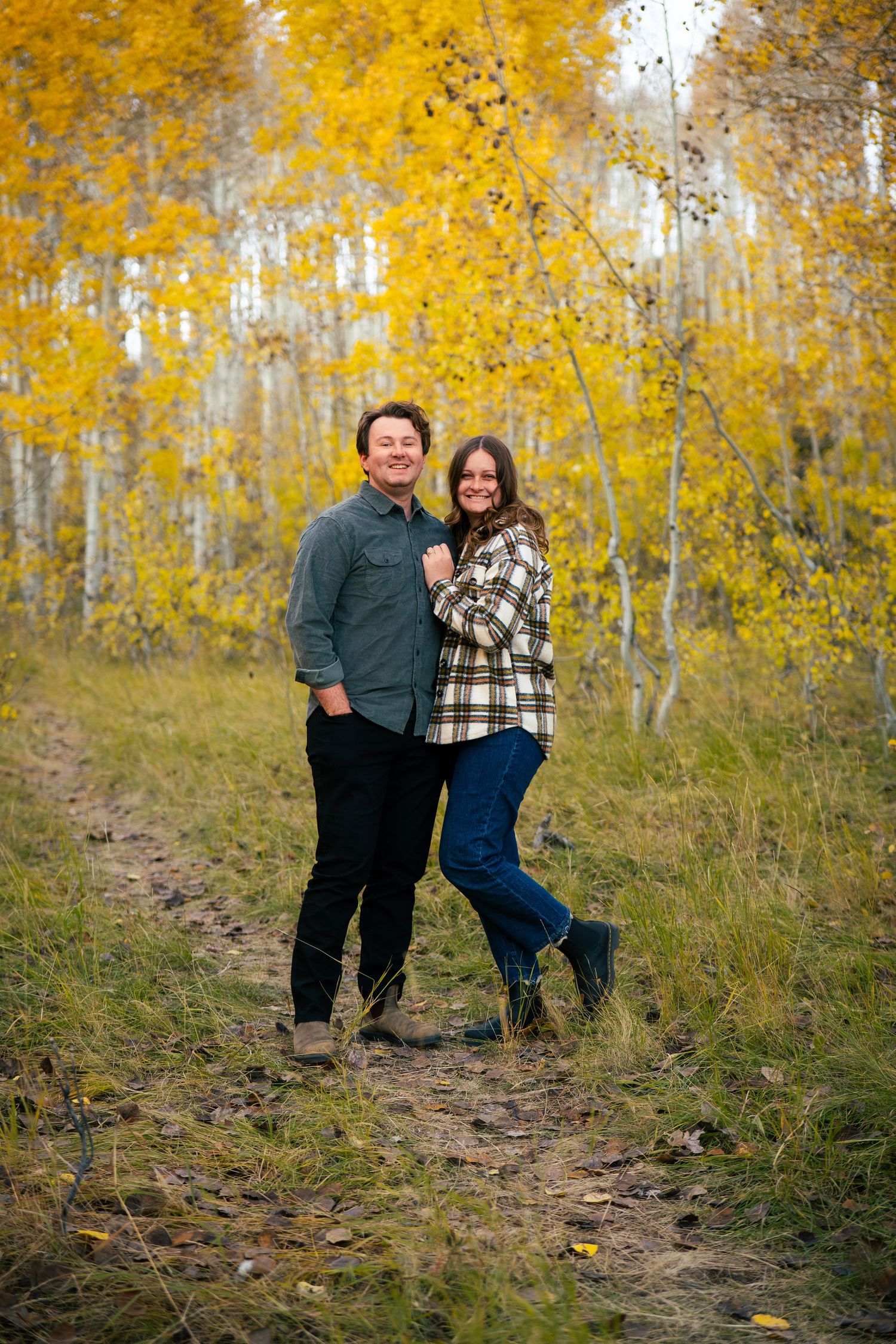 Couple embracing on a forest path surrounded by golden autumn aspen trees in a romantic fall outdoor portrait.