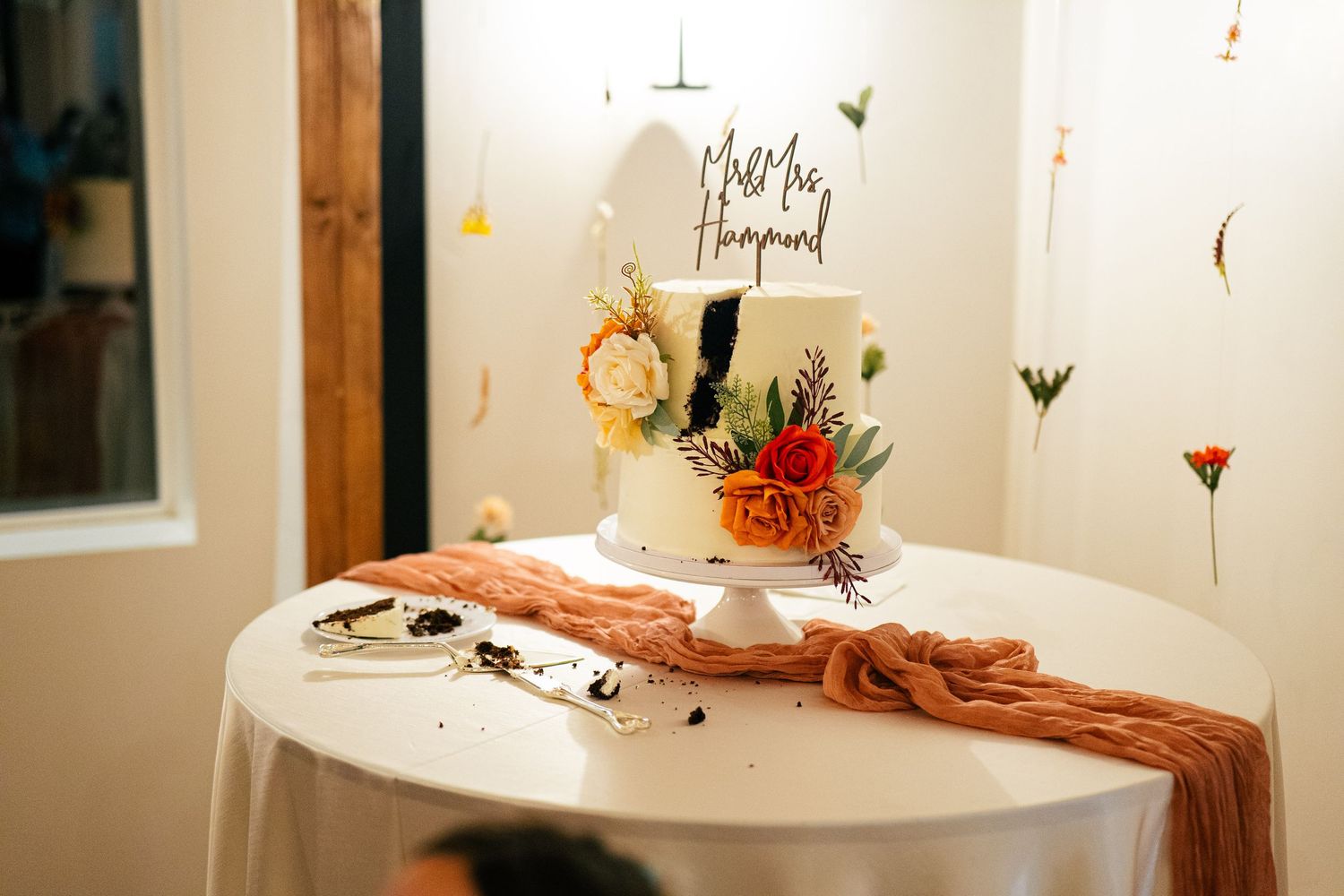 Two-tier white wedding cake with colorful floral decorations and a Mr. and Mrs. topper on a draped table.