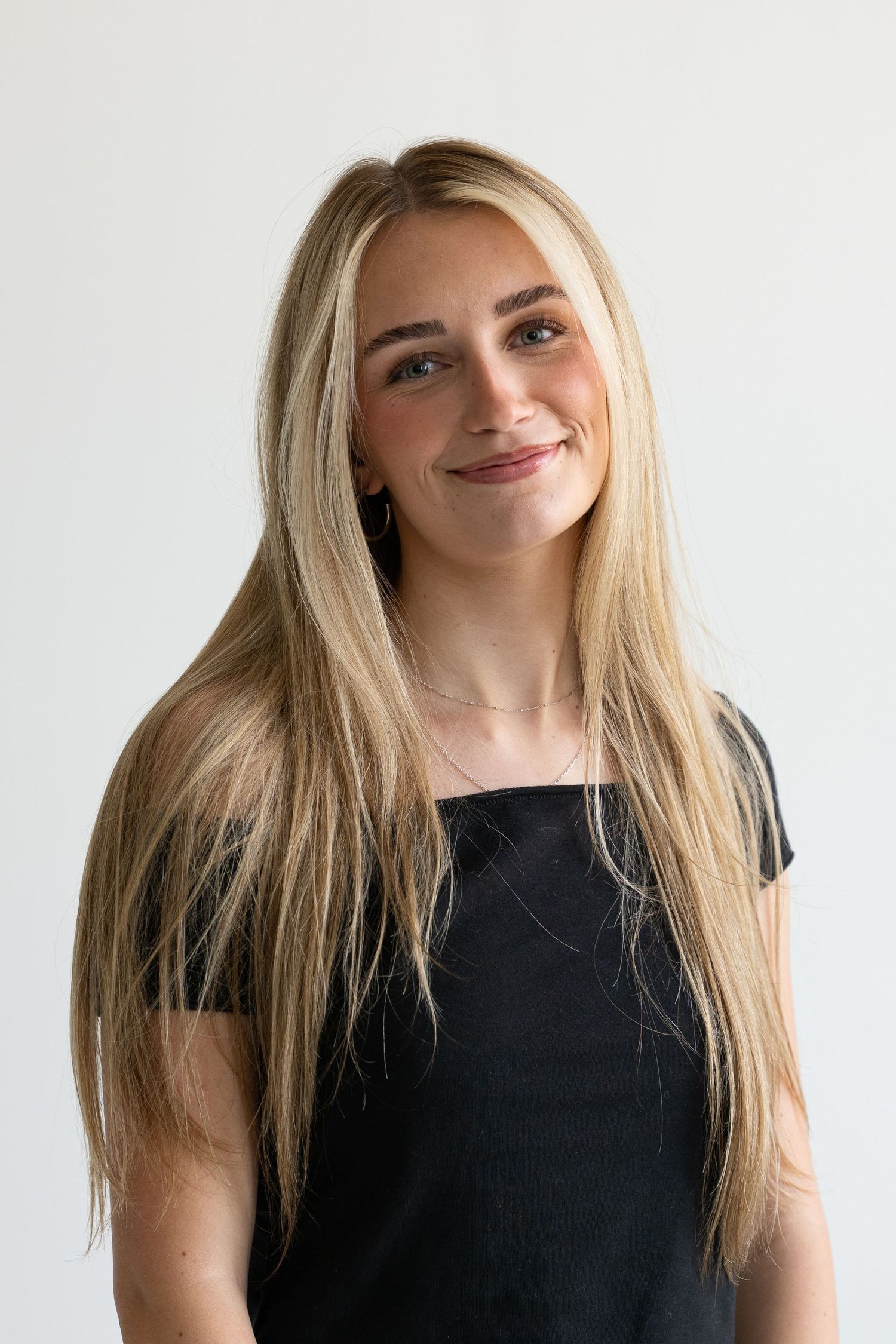 Young woman with long blonde hair smiling in a black top against a white background.