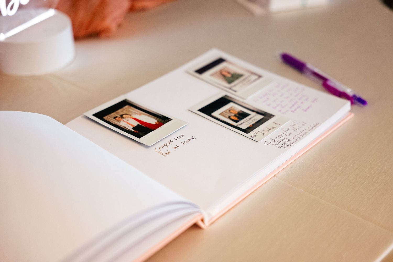 Open wedding guest book with Polaroid photos and handwritten notes, purple pen on white table.