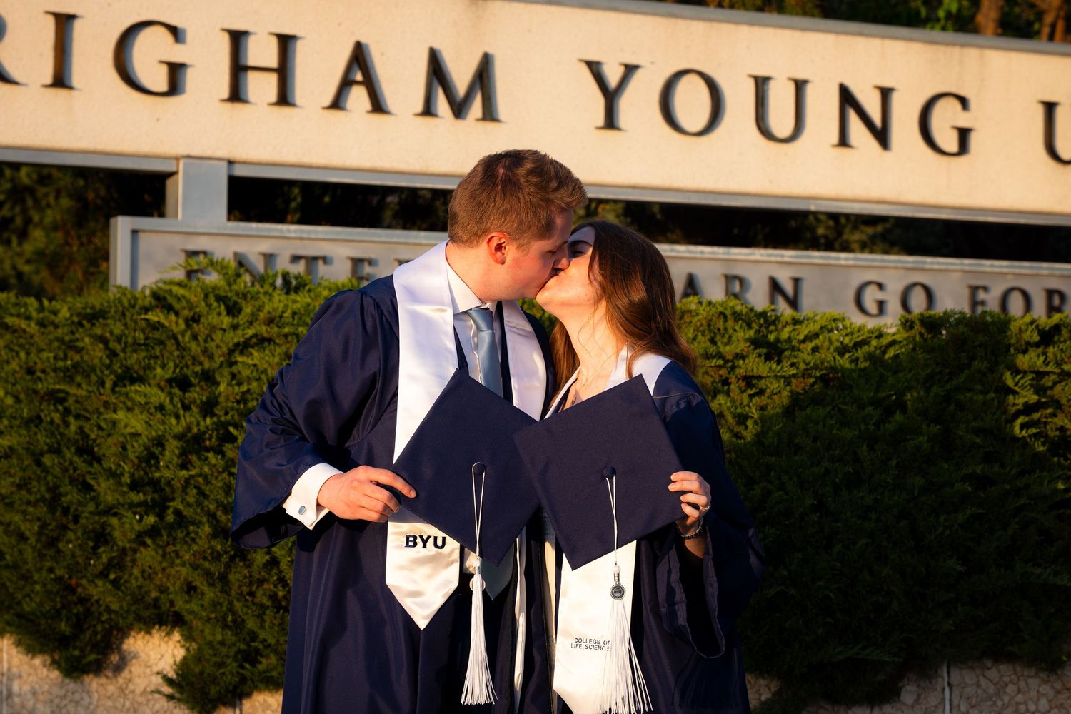 A couple in graduation gowns and caps stand together in front of a university building.