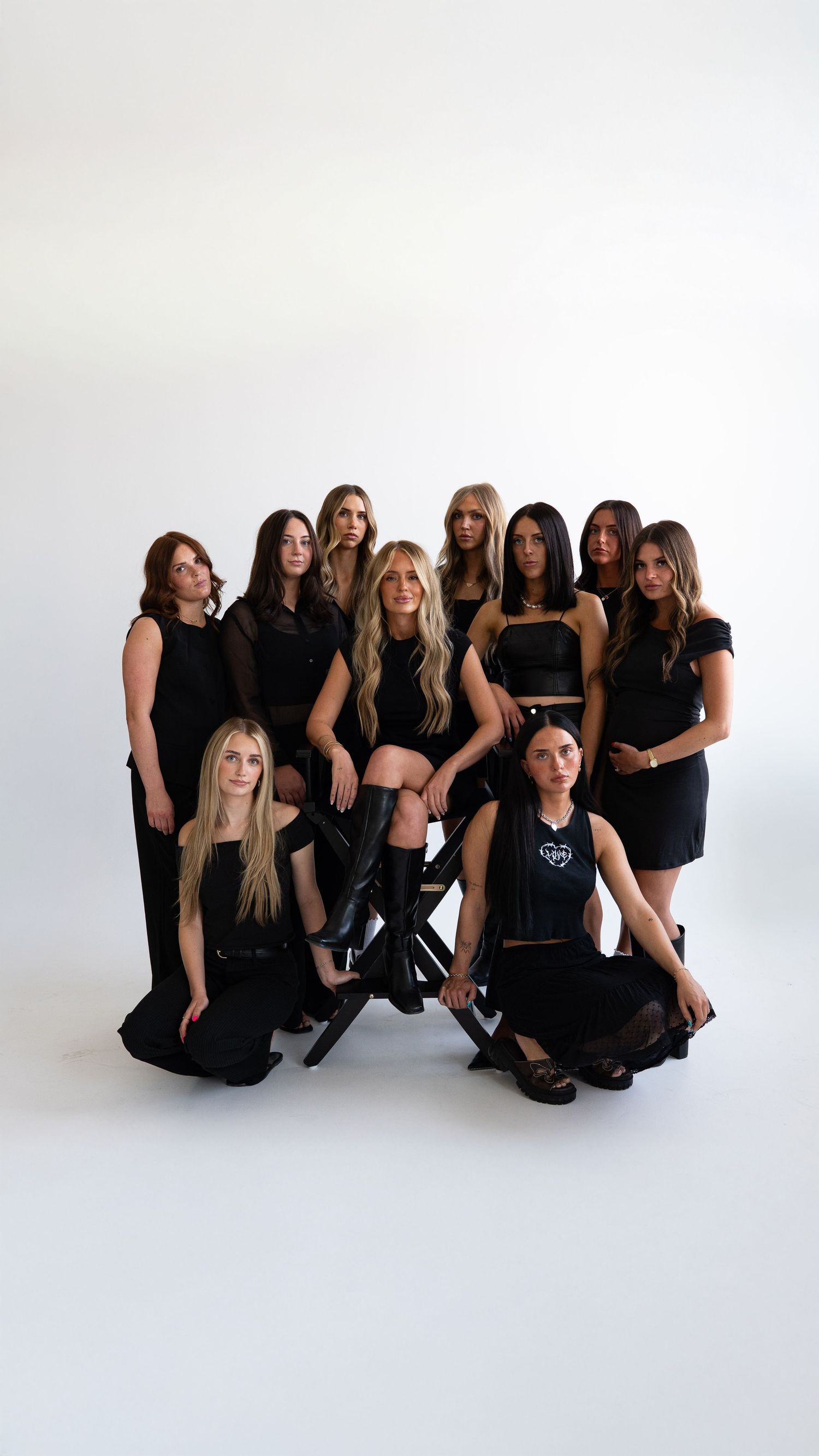 Group of ten women posing together in coordinated black outfits against a white studio background.