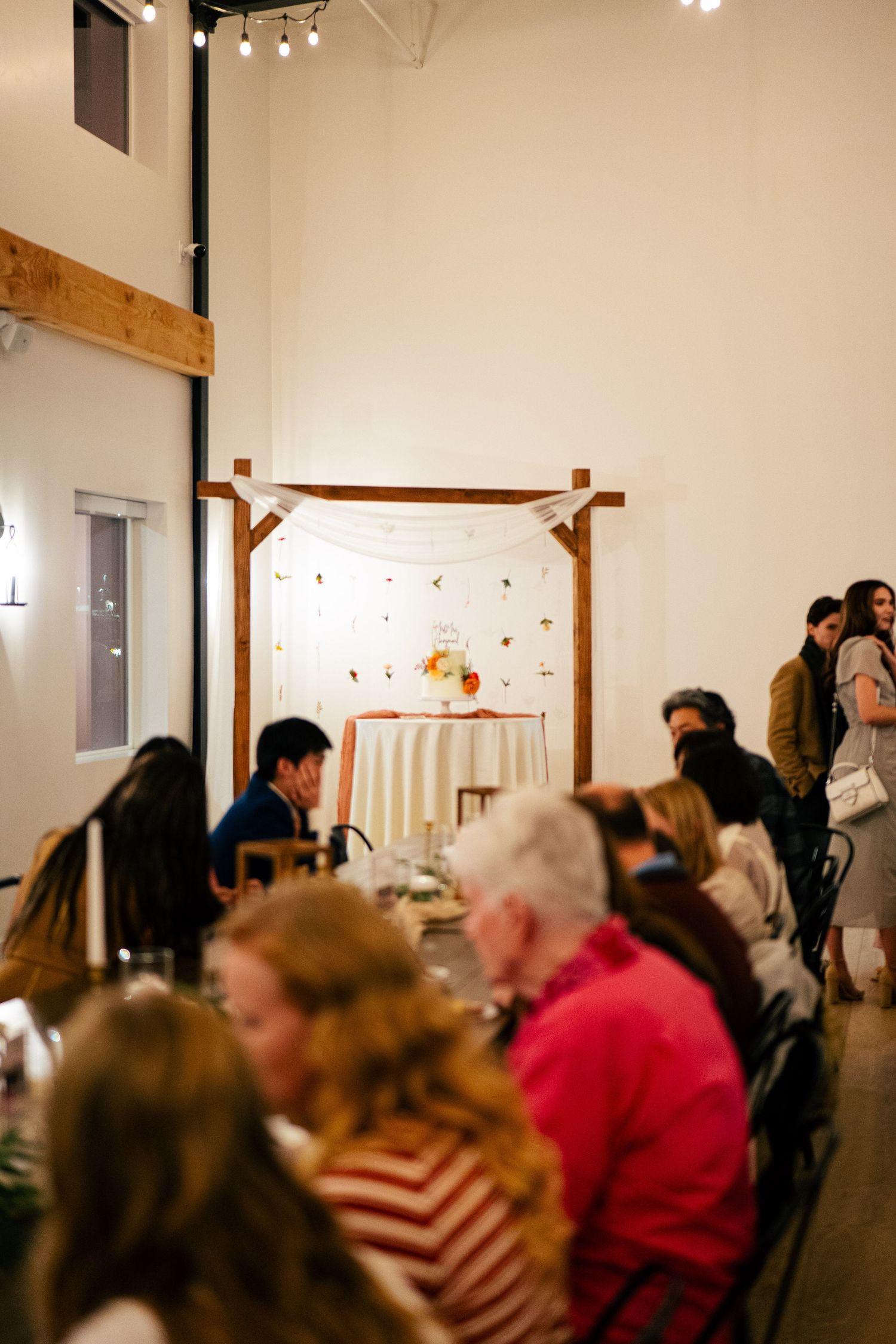 Guests seated at long tables during a rustic wedding reception with wooden arch backdrop.