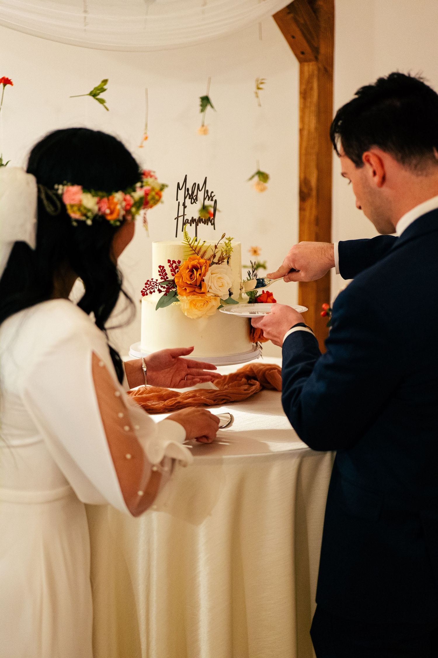 Bride and groom cutting a white floral wedding cake together at their reception venue.