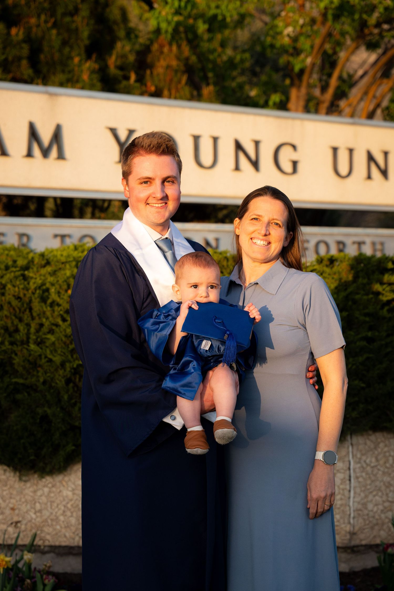A family of four, including two adults and two children, pose for a graduation photo outdoors.