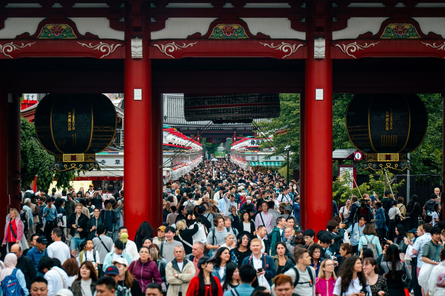 A crowded street scene with a large red gate and traditional Japanese architecture, with a large crowd of people.