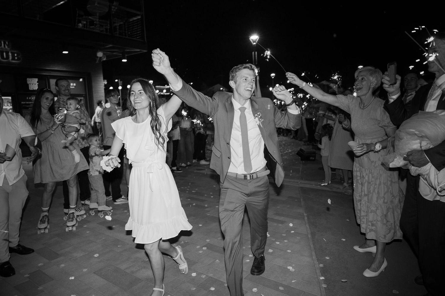 Black and white photo of a joyful bride and groom dancing outdoors at night during their wedding sendoff.