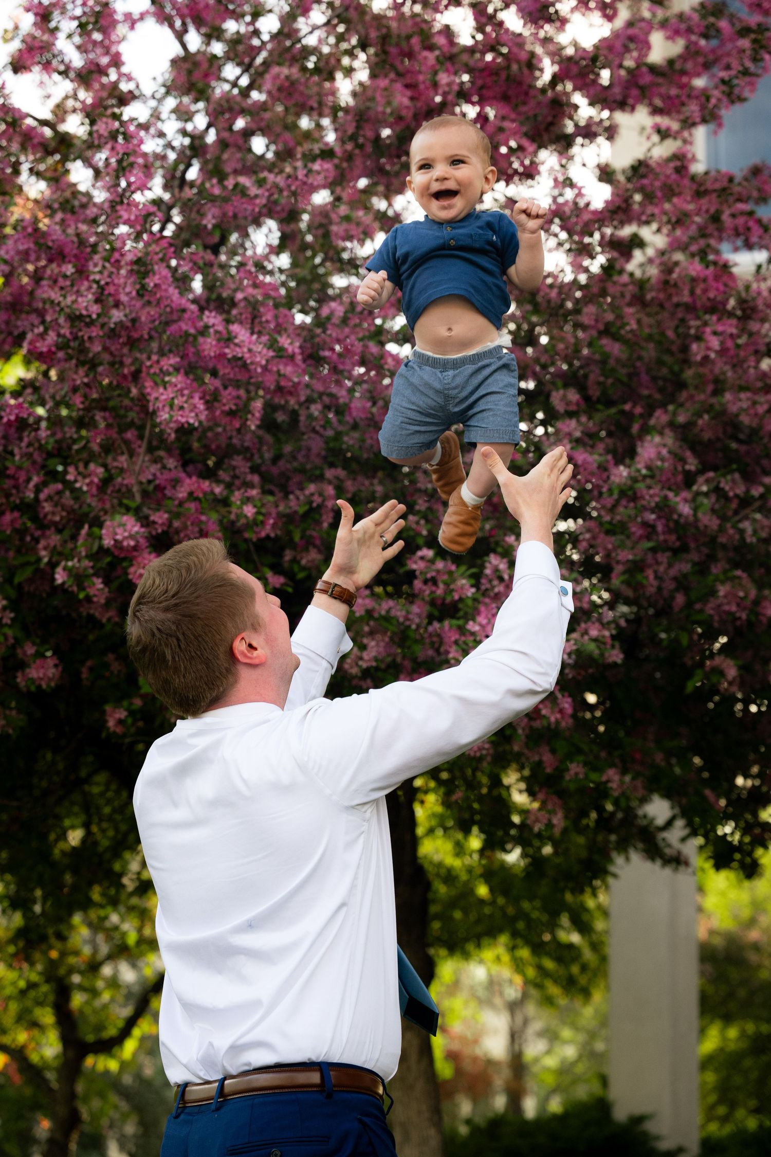 A woman holds a young child in her arms in a park with blooming trees.
