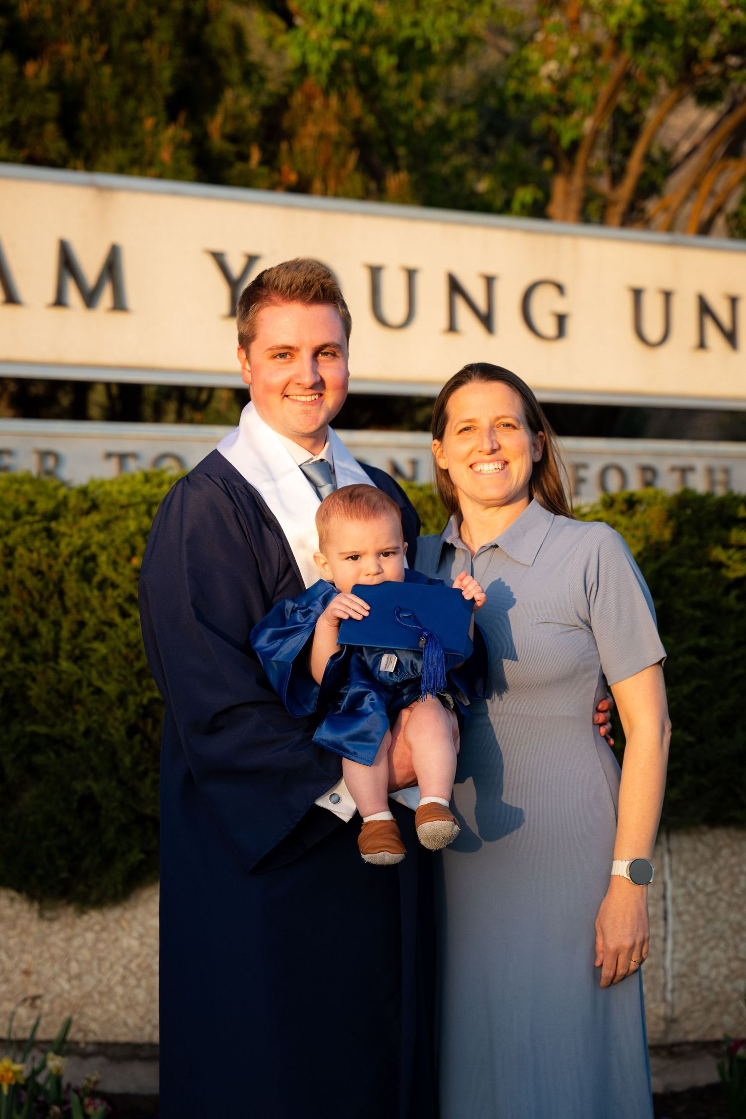 A family, including a man, woman, and baby, stand in front of a university building.
