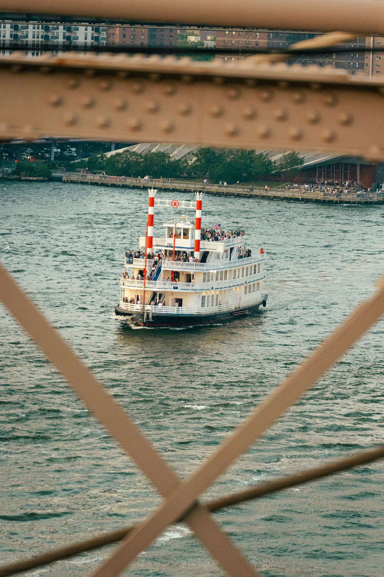 A passenger ferry boat is sailing on a body of water, framed by a metal structure in the foreground.