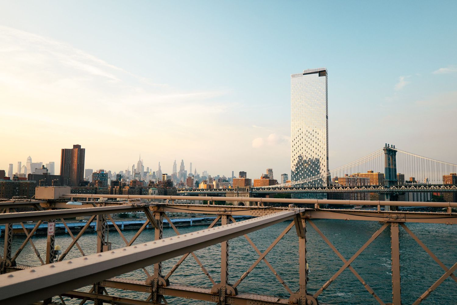 A cityscape with skyscrapers and bridges overlooking a body of water, with a clear sky in the background.