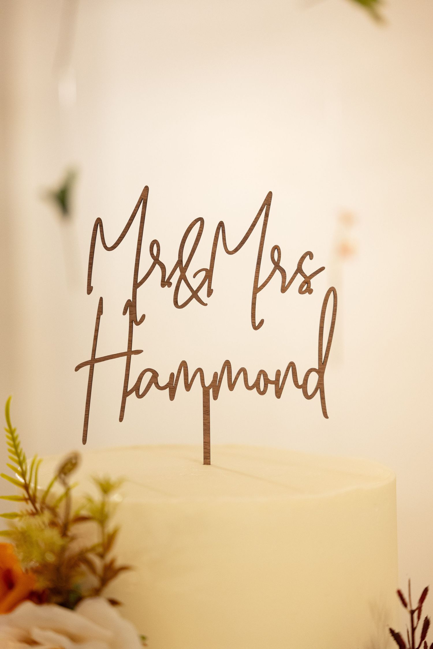 Mr and Mrs Hammond wooden cake topper on white wedding cake with floral decor.