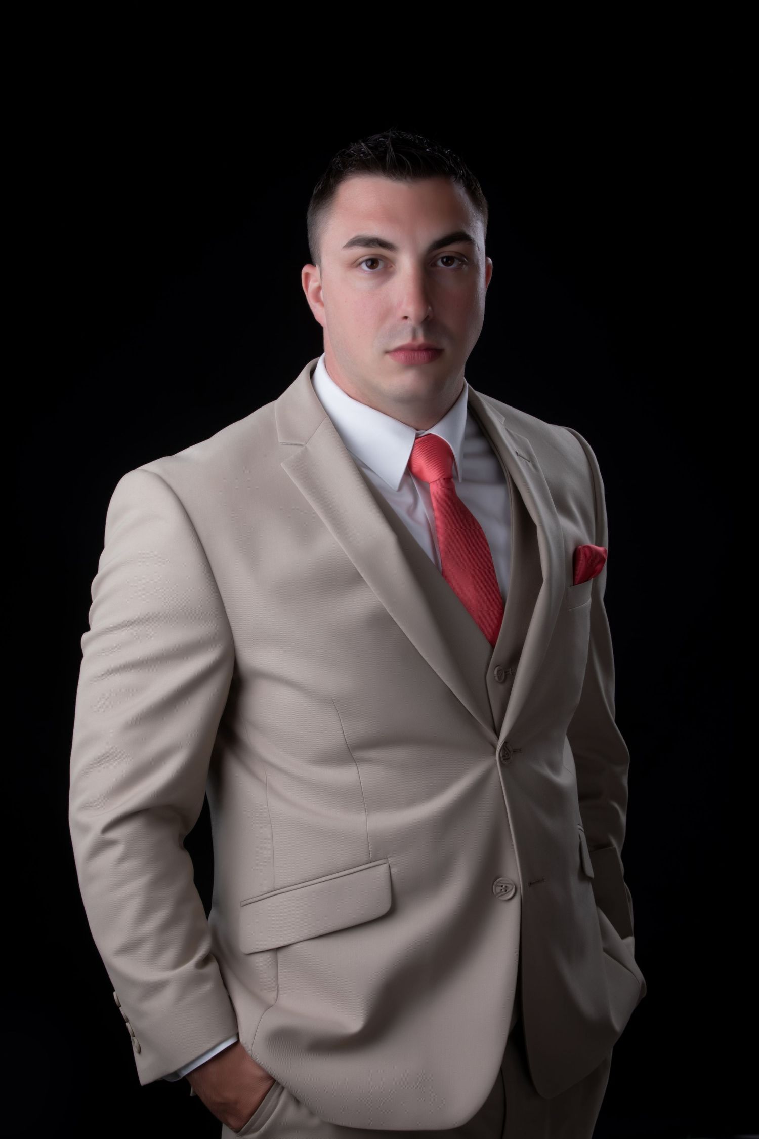 Professional headshot of man in beige suit against black background.