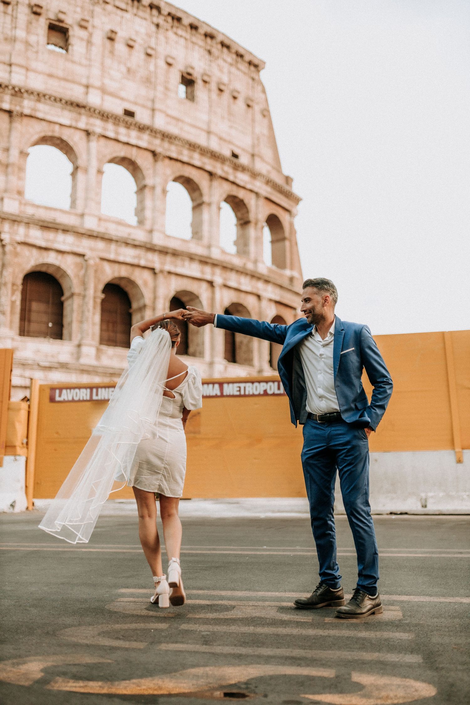 Couple in wedding attire dancing in front of the Colosseum in Rome, Italy.